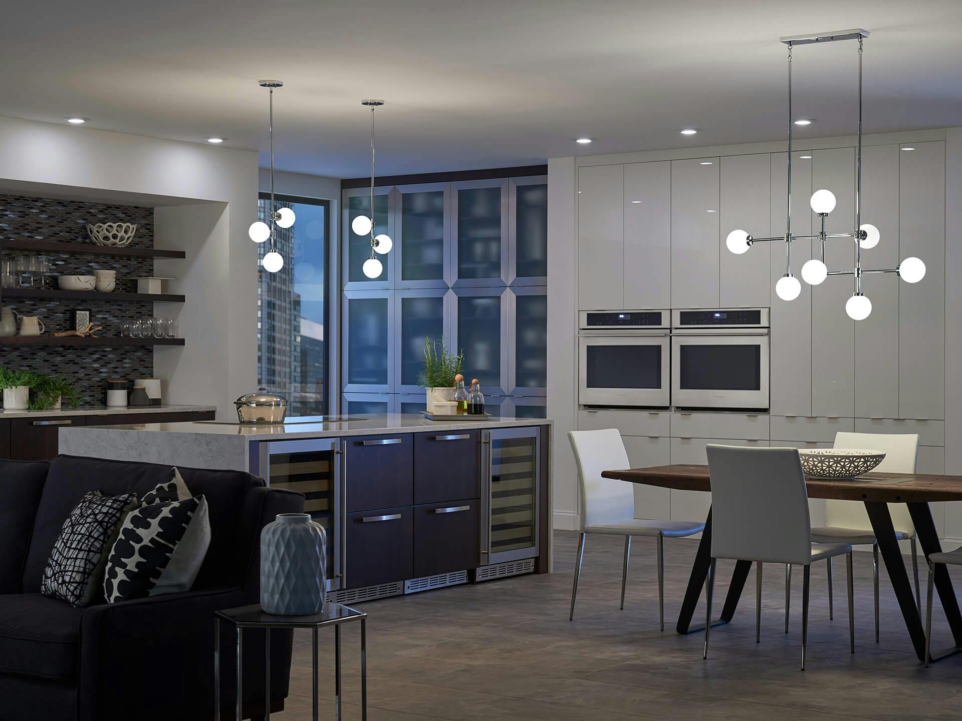High rise open concept apartment at night with Aura chandelier and pendant lights hanging over a dining table and kitchen island