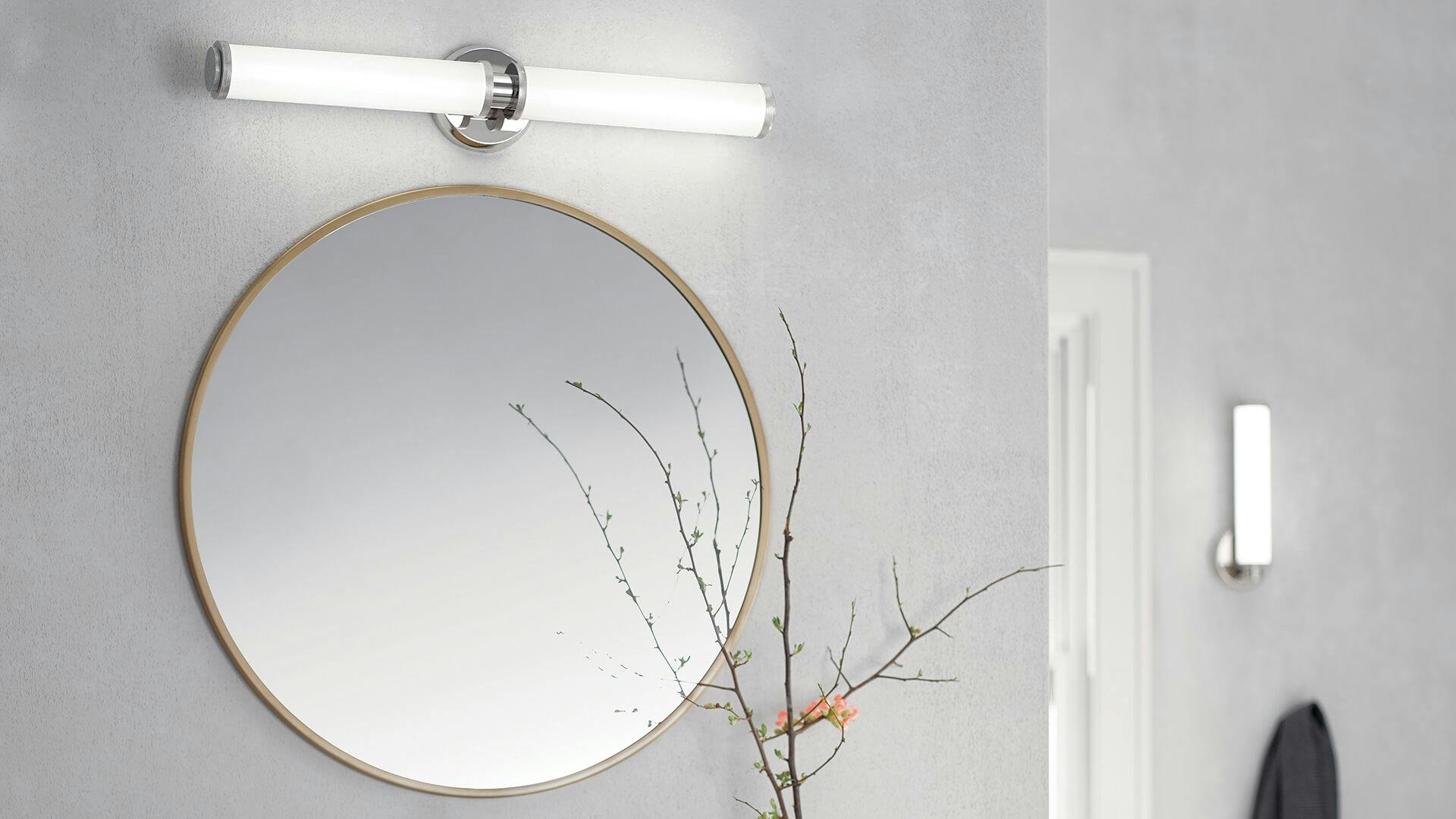 White bathroom wall featuring a mirror with a Indeco vanity light above it and a wall sconce in the background