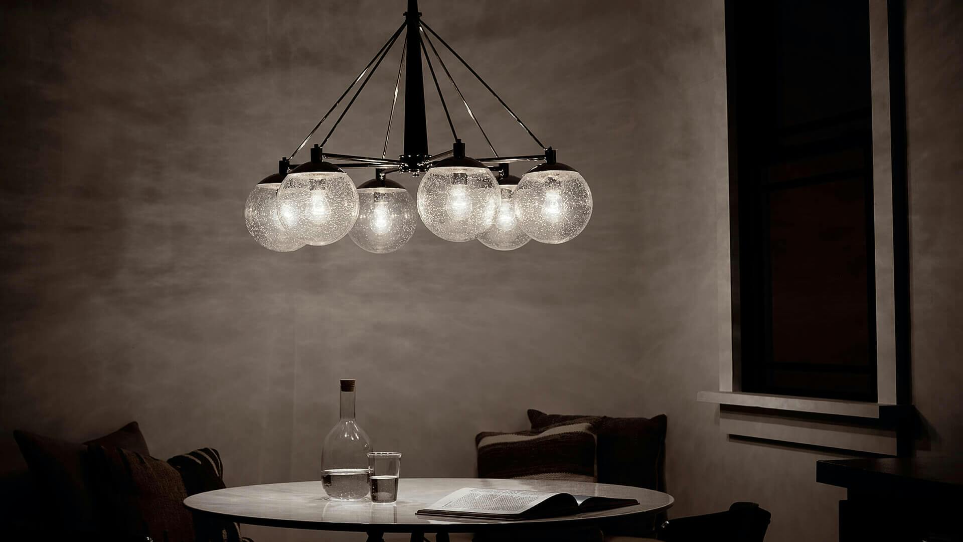 Dining table in a dark grey corner of the kitchen, an illuminated Marilyn chandelier hangs above the able