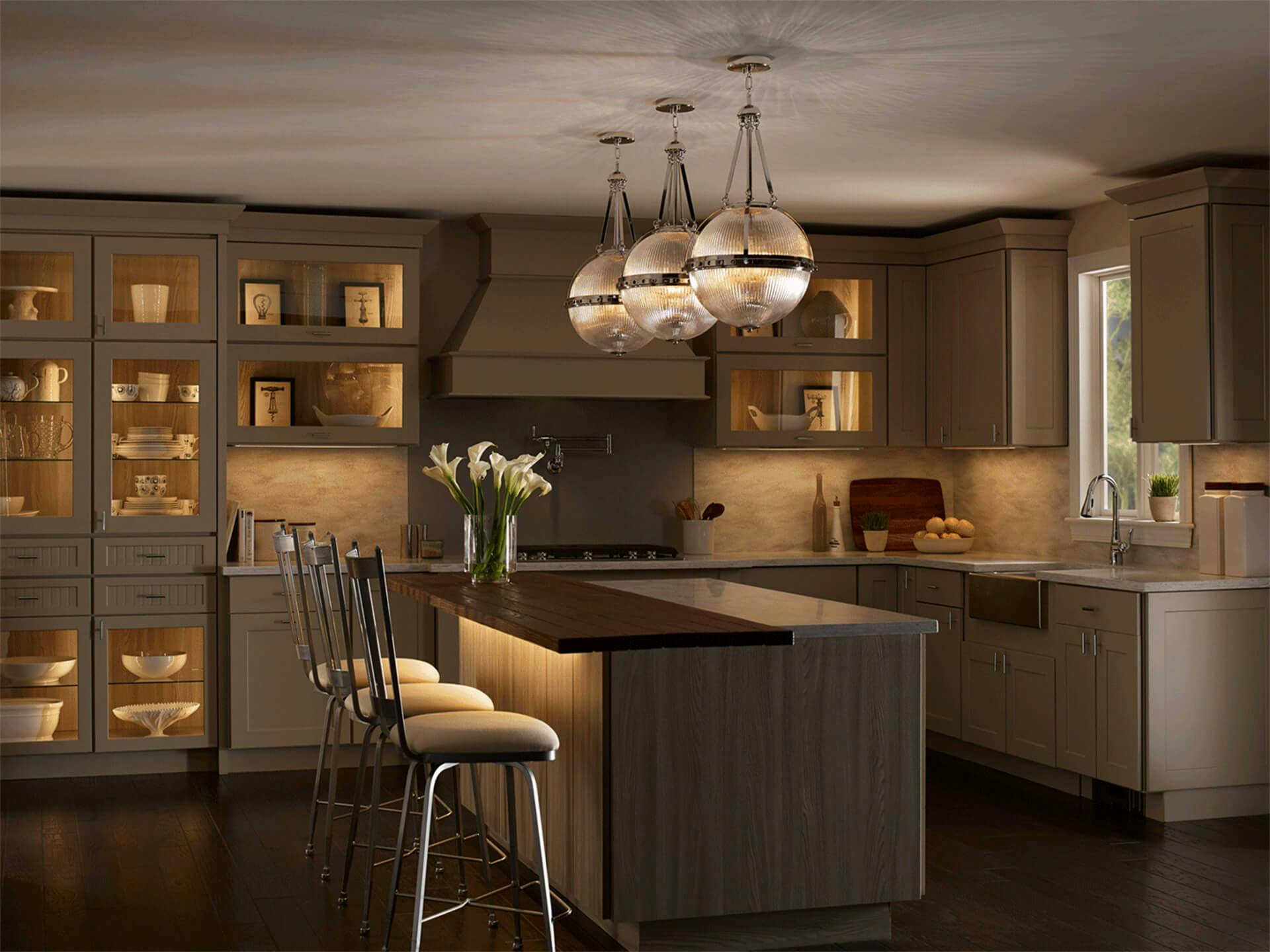 Dark scene of a kitchen with three Aster pendants hanging above the island and 6U Series LED Under Cabinet Lighting illuminating nearby chairs