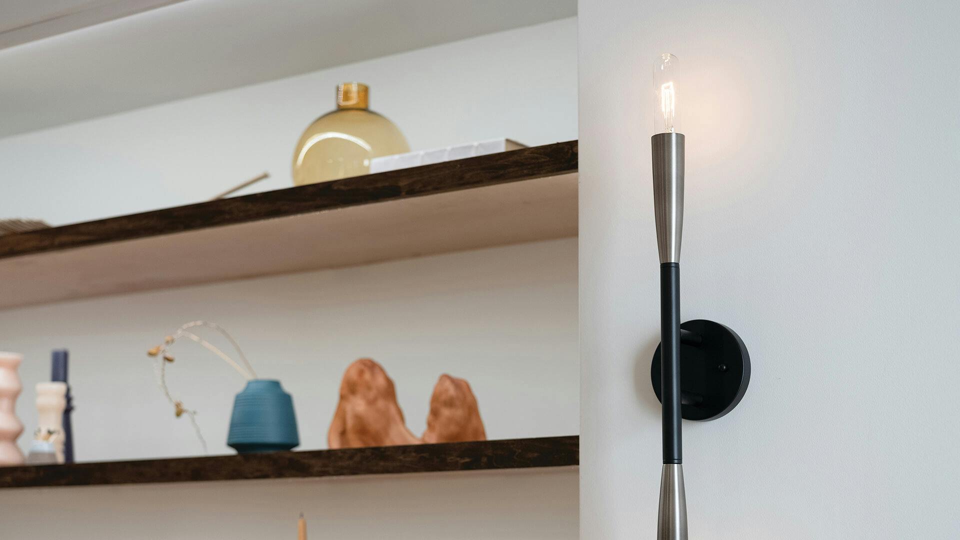 Shelving with various items on them with a lit Branches sconce nearby