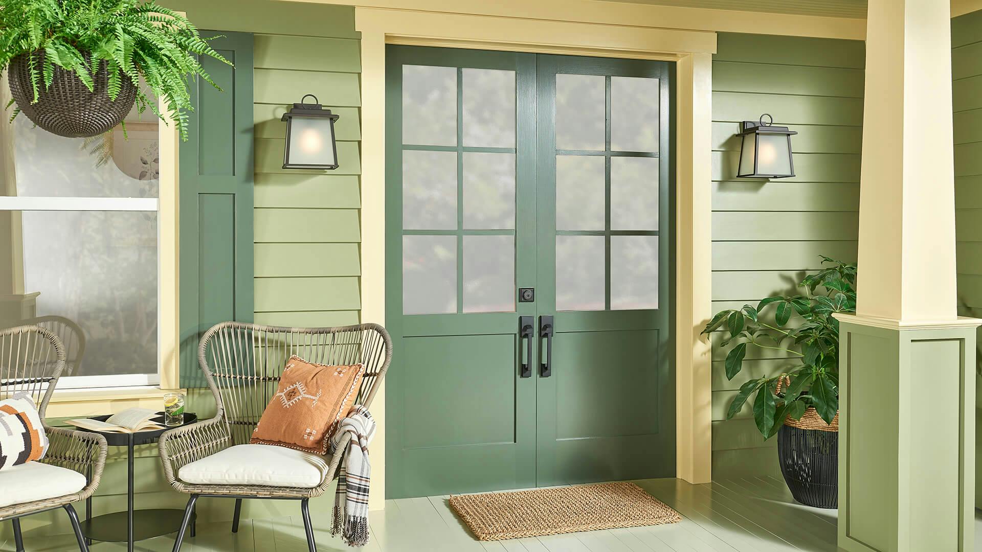 Exterior of a patio painted in different shades of green, featuring two Noward sconces on either side of the front doors