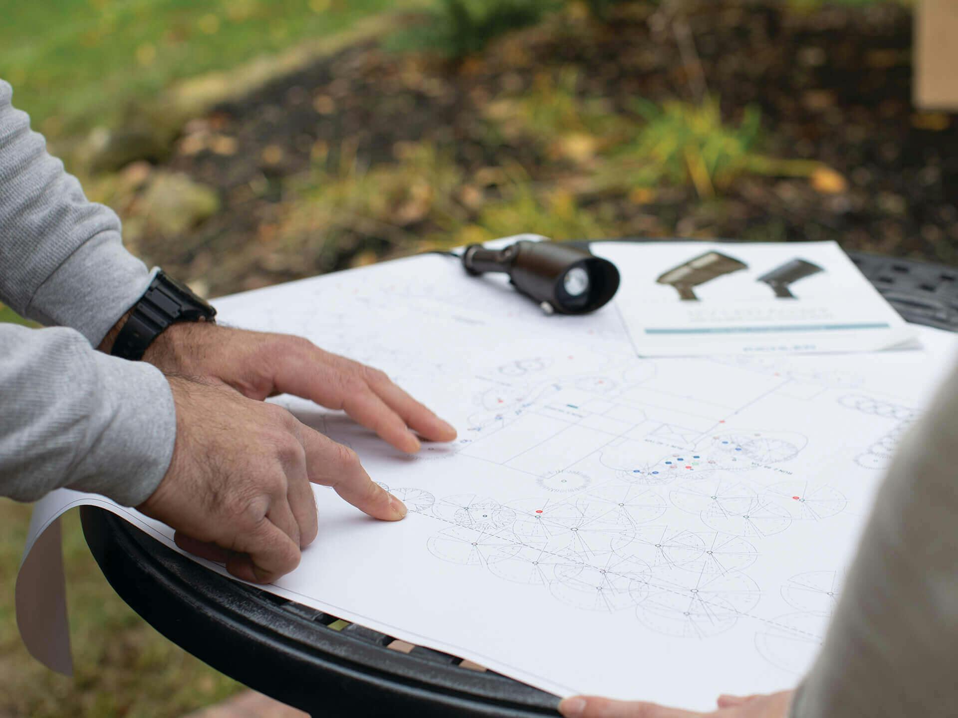 Close up of hands working on a blueprint on an outdoor garden table