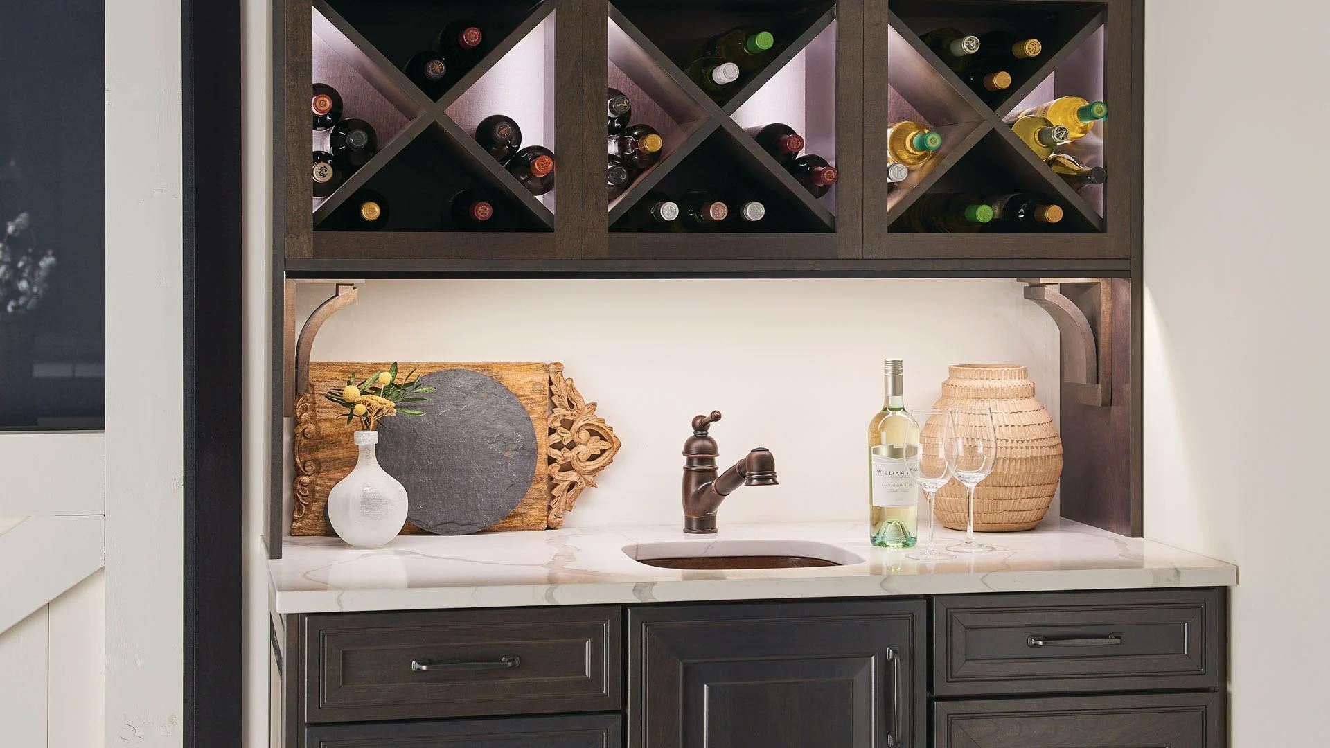 Close up on a cabinet holding multiple wine bottles with a built in sink featuring under cabinet lighting.