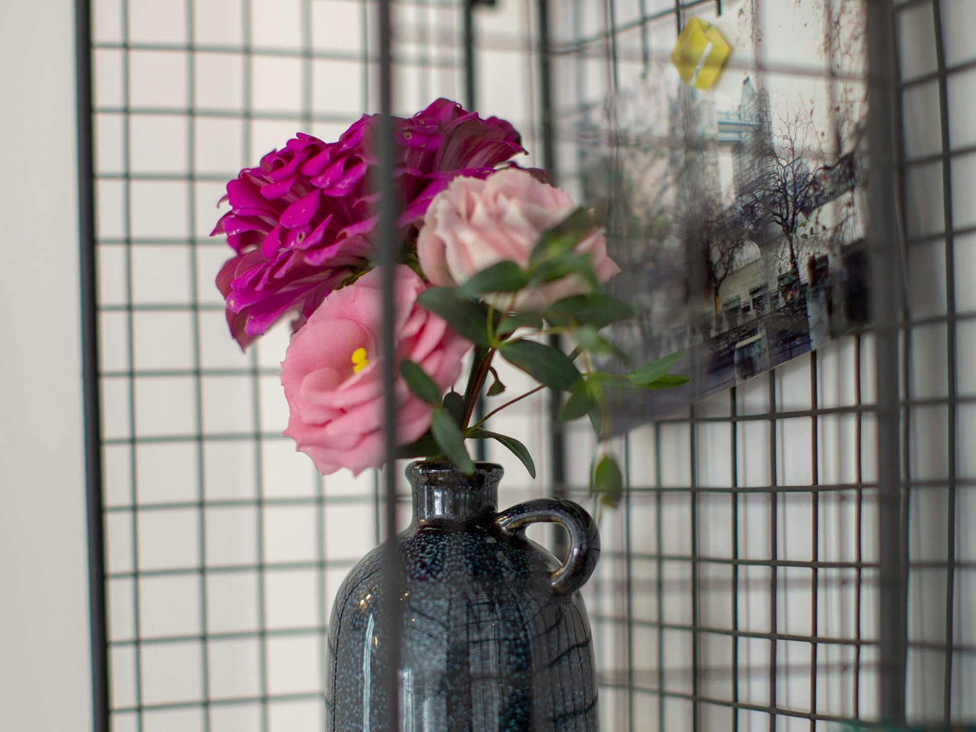 Close up of a ceramic blue jug with purple and pink flowers on a black grated shelf