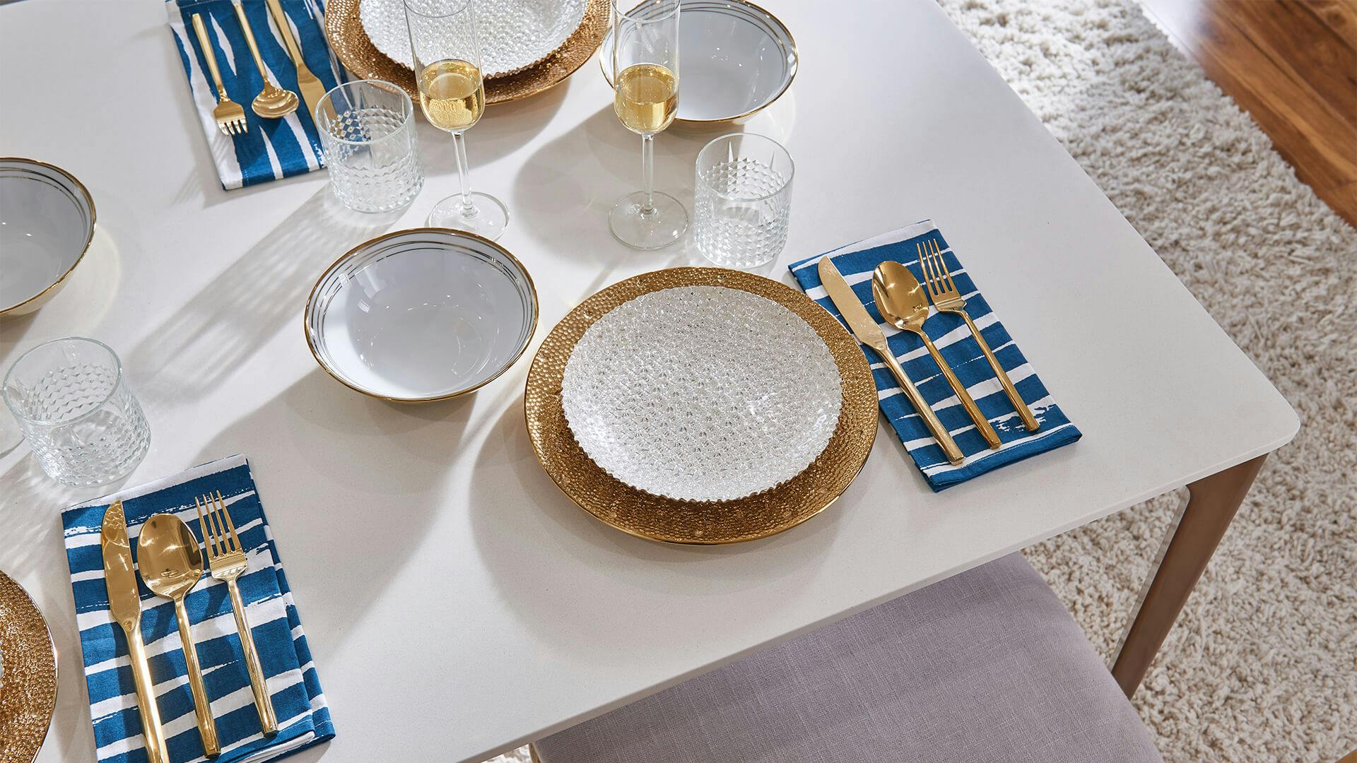 Table setting with white plates accented by gold flatware atop deep blue napkins and a bright wine
