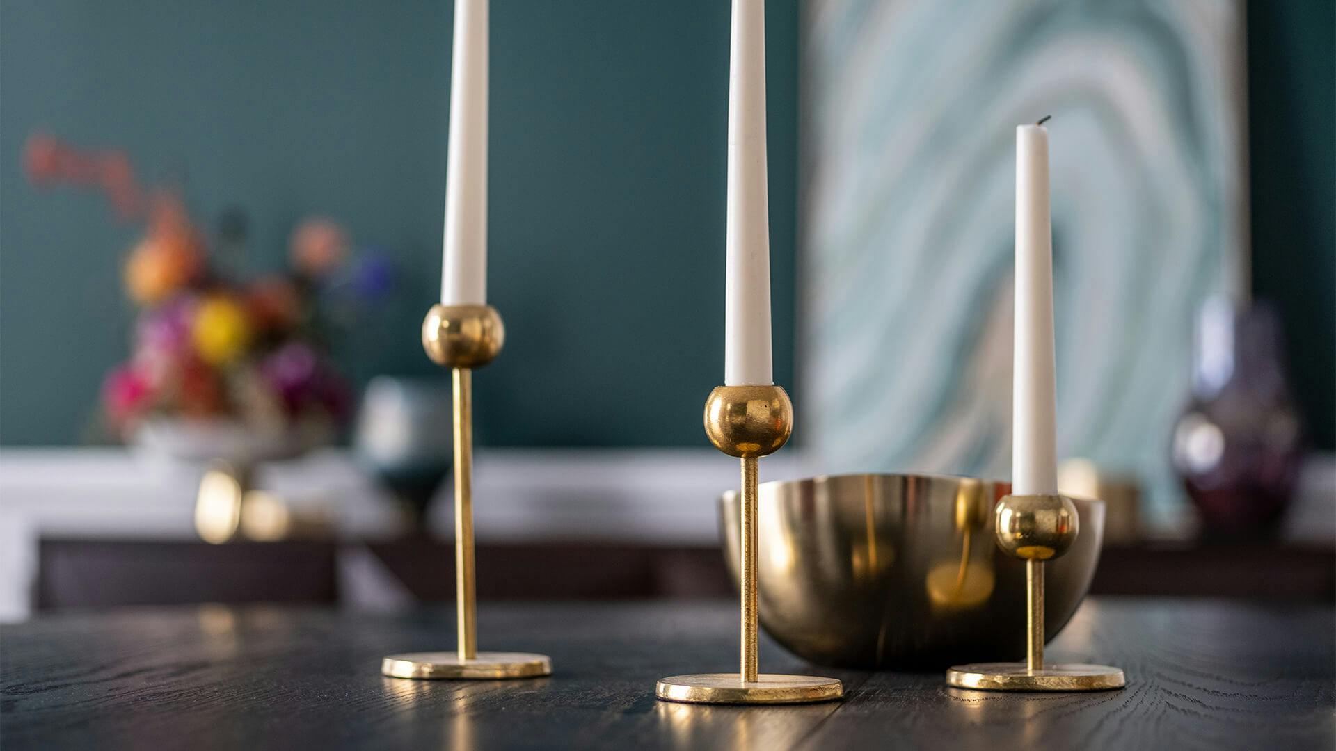 Brass candle holders with white candles and brass bowl on table top.