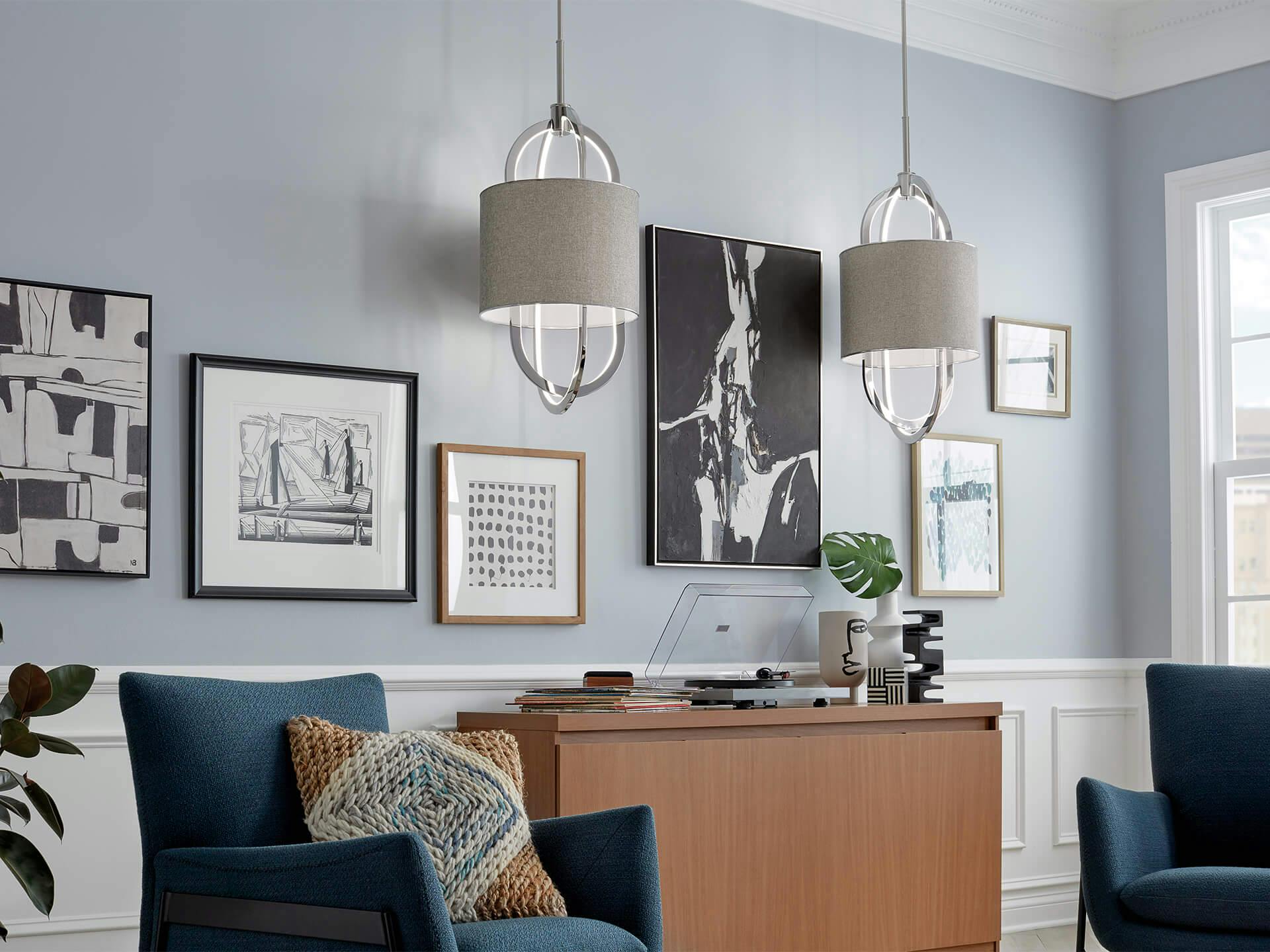 A living room with framed artwork on a neutral grey painted wall lit with two Jolana pendants in the daytime 