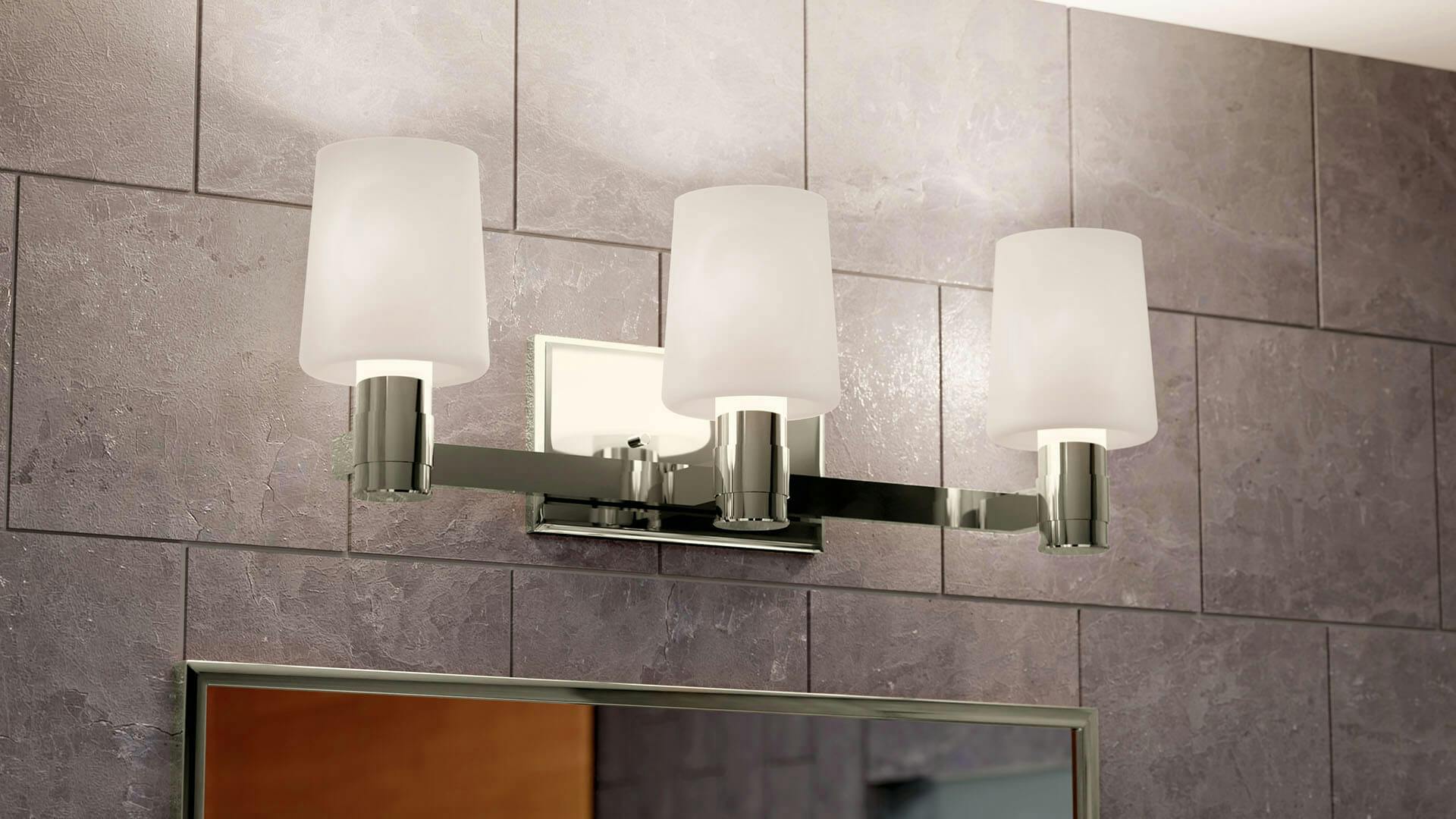 Close up of a three light adani wall sconce vanity light over a bathroom mirror.