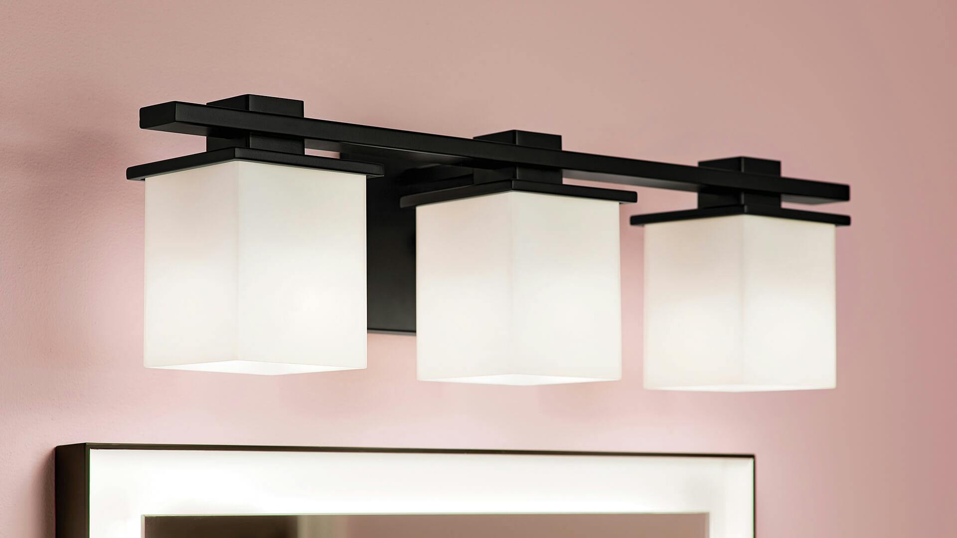 Close up of a Tully sconce light in black finish above a bathroom mirror with a pale pink wall