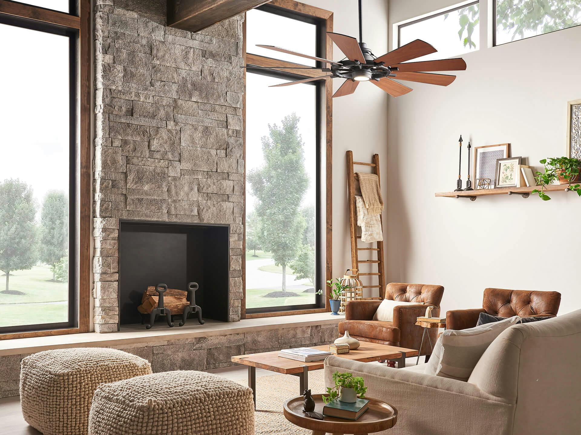 Living room with floor to ceiling windows and large stone fireplace, featuring a Gentry ceiling fan