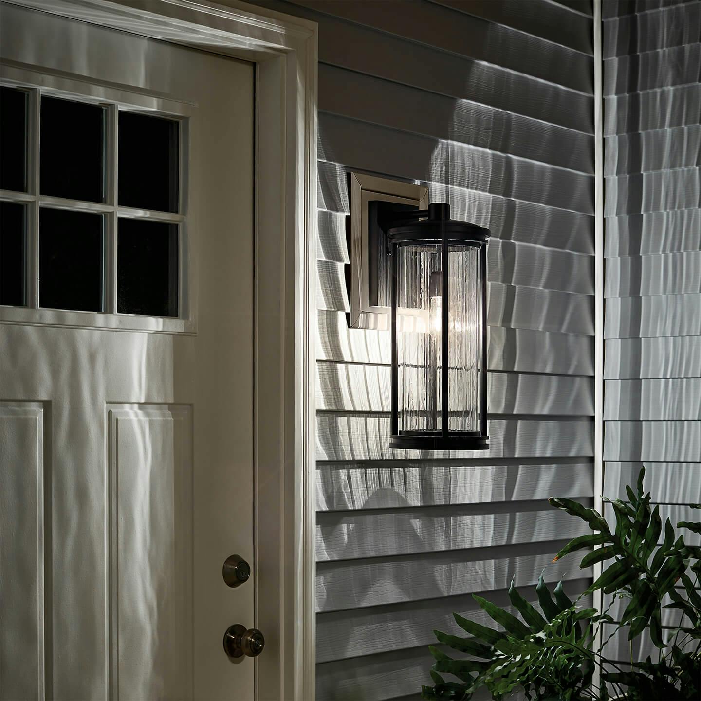 A Barras exterior wall light mounted to the side of a side door of a white house turned on at night
