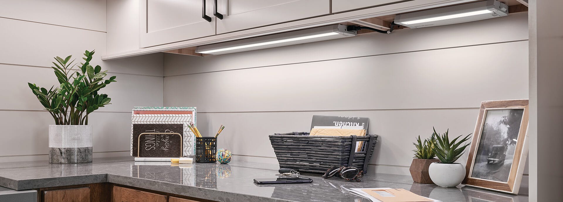 Cabinets with lighting underneath above a grey counter with various decorative items.