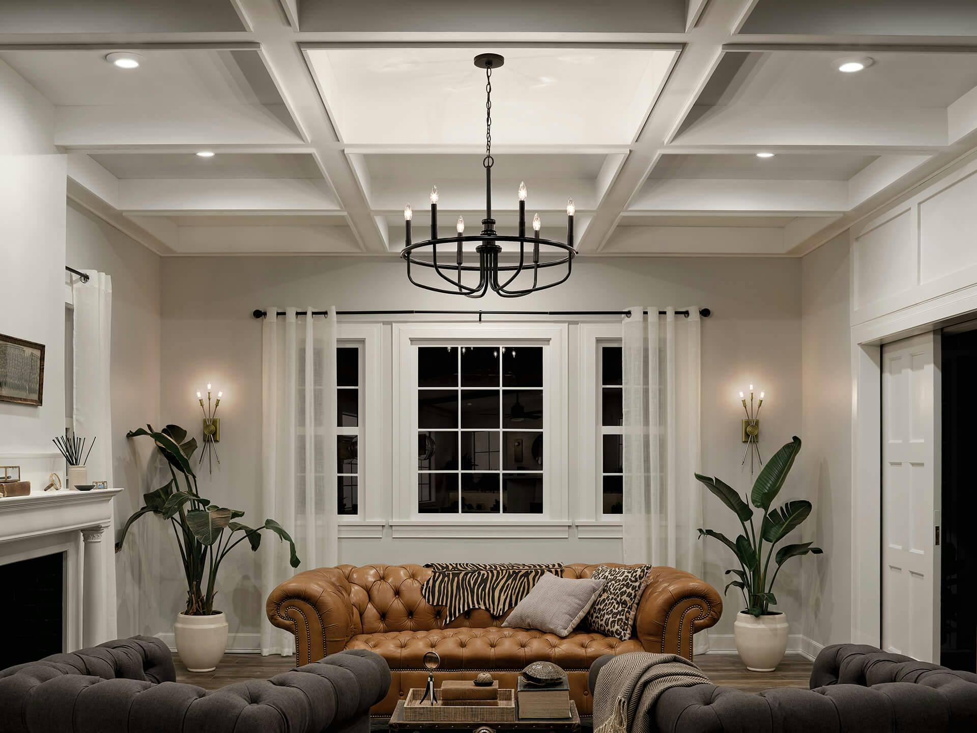 A white living room with tall, grid-like ceiling featuring downlighting throughout along with a Capitol Hill chandelier in the center and two Doncaster sconces on the back wall