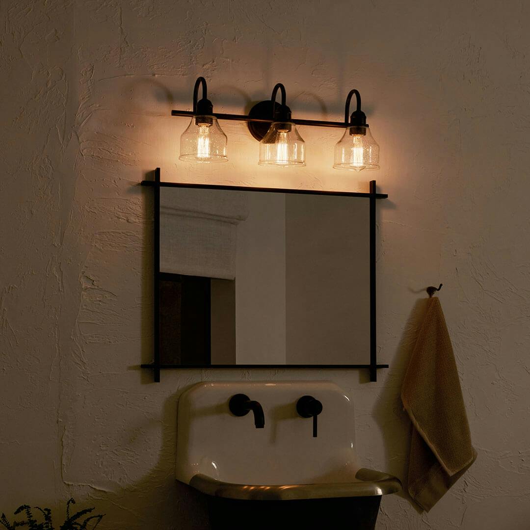 Bathroom at night with the Avery 24 Inch 3 Light Vanity Light with Clear Seeded Glass in Black