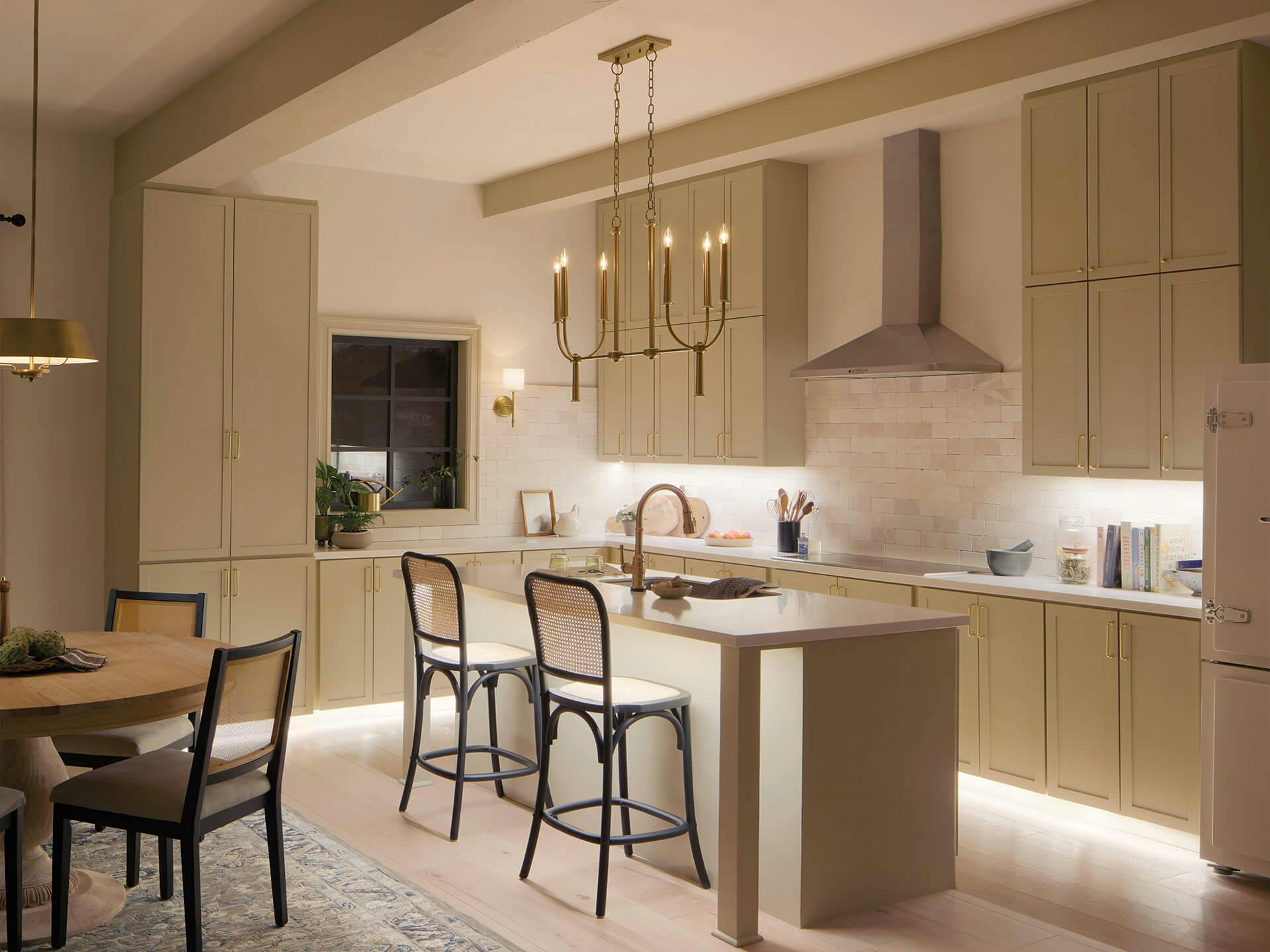 Beige kitchen at night with a Florence 6-light chandelier hanging over the island in brushed natural brass