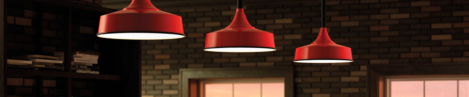 three red commercial lighting pendants hanging in front of a brick wall