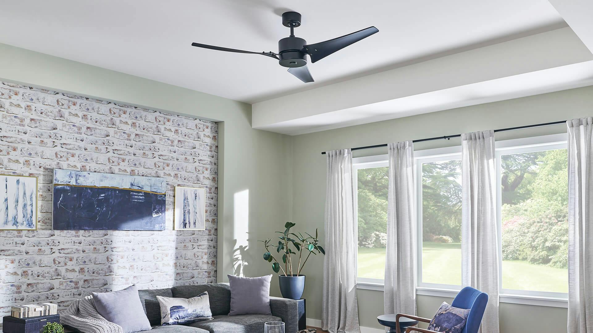 Living room with Motu ceiling fan in black finish during the day with three windows and grey couch