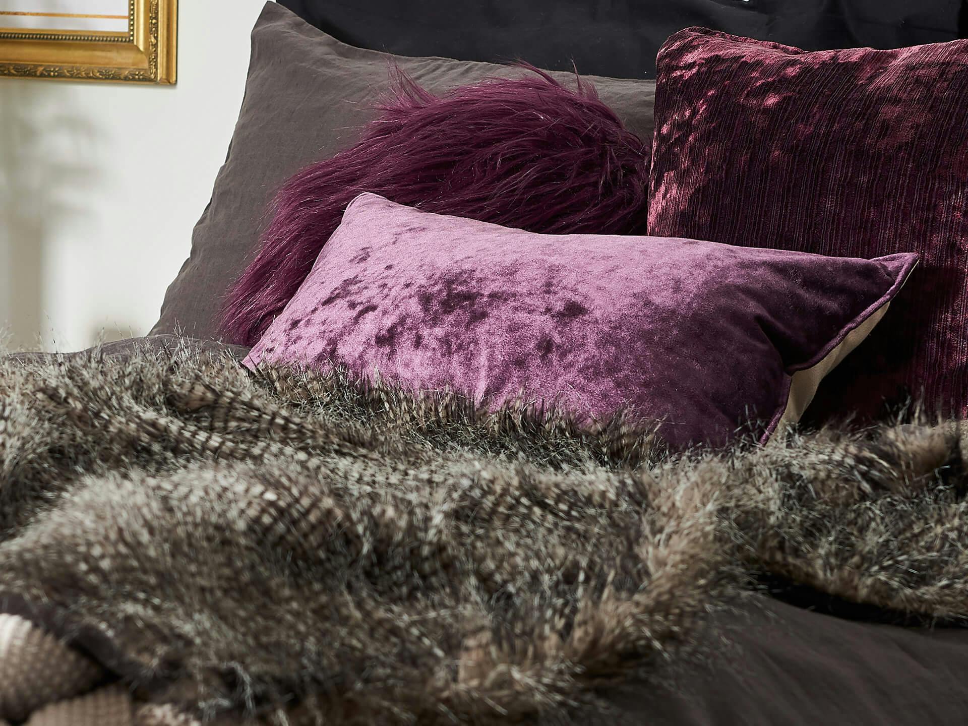 Close up of a bed with dark purple throw pillows and dark sheets