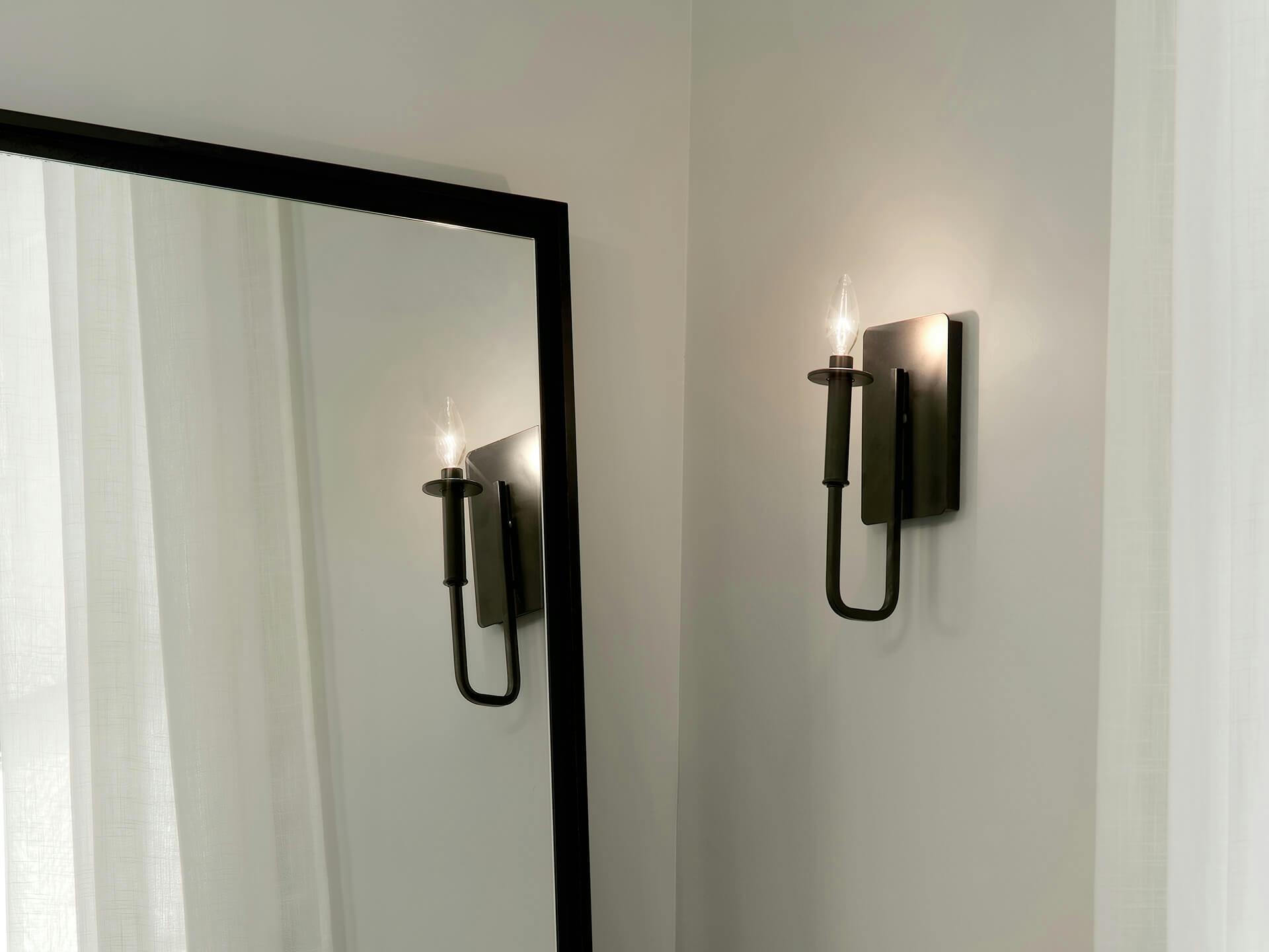 Close up of an Alden black finish wall sconce next to a corner mirror