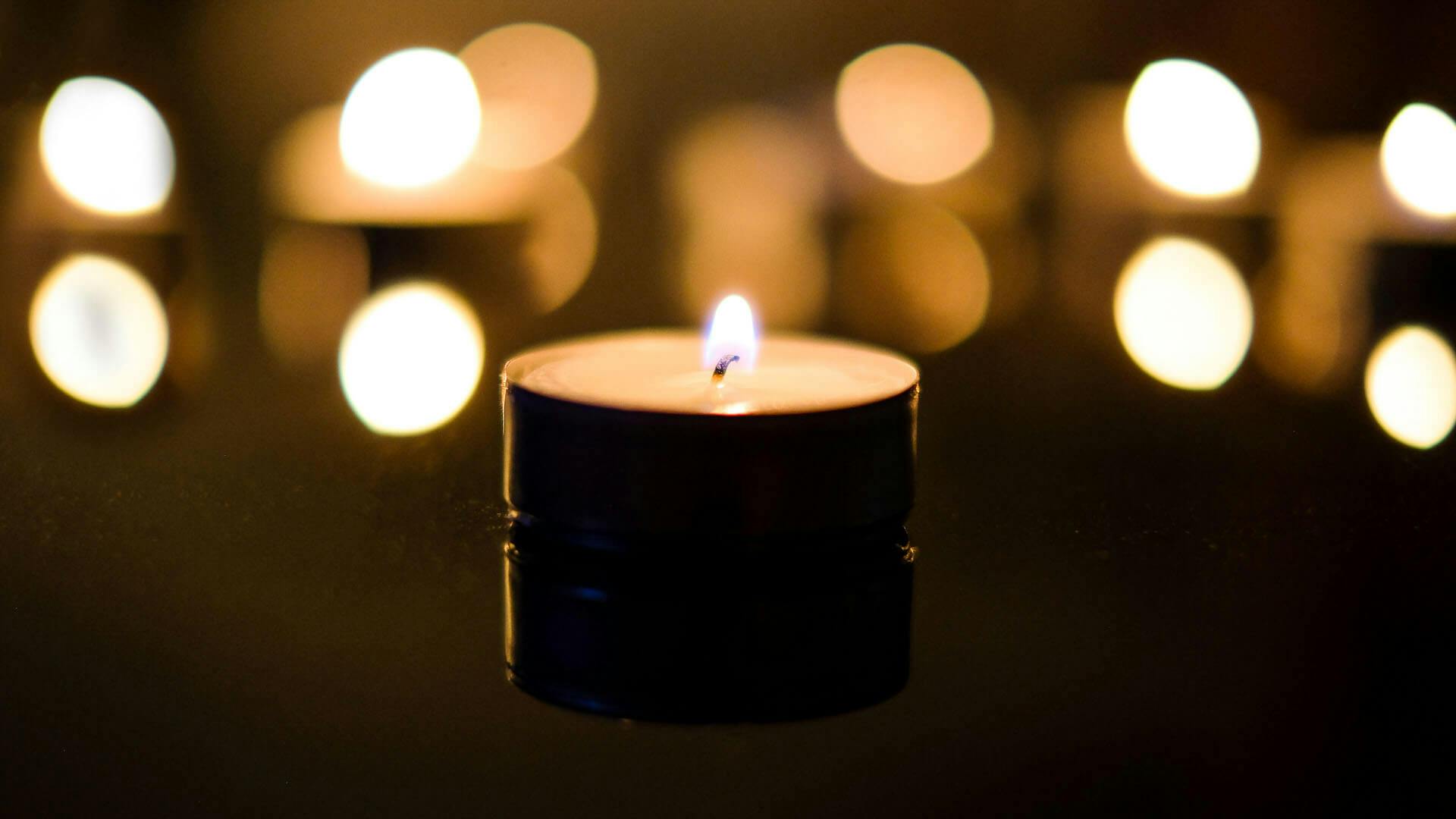 Close-up of a lit candle in a dark room with bokeh of other candles in the background
