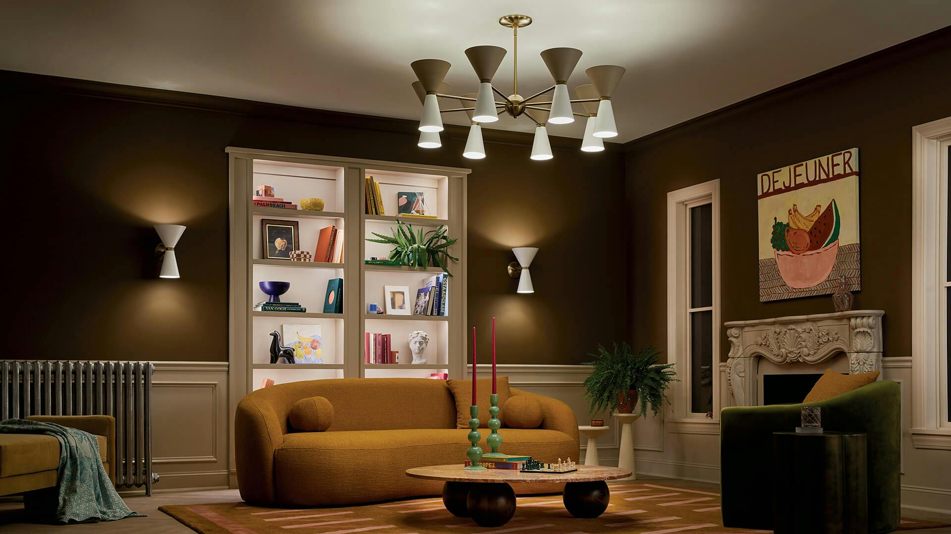 Living room with dark green walls, yellow couch, built in shelves at night with a white and gold Phix chandelier in center