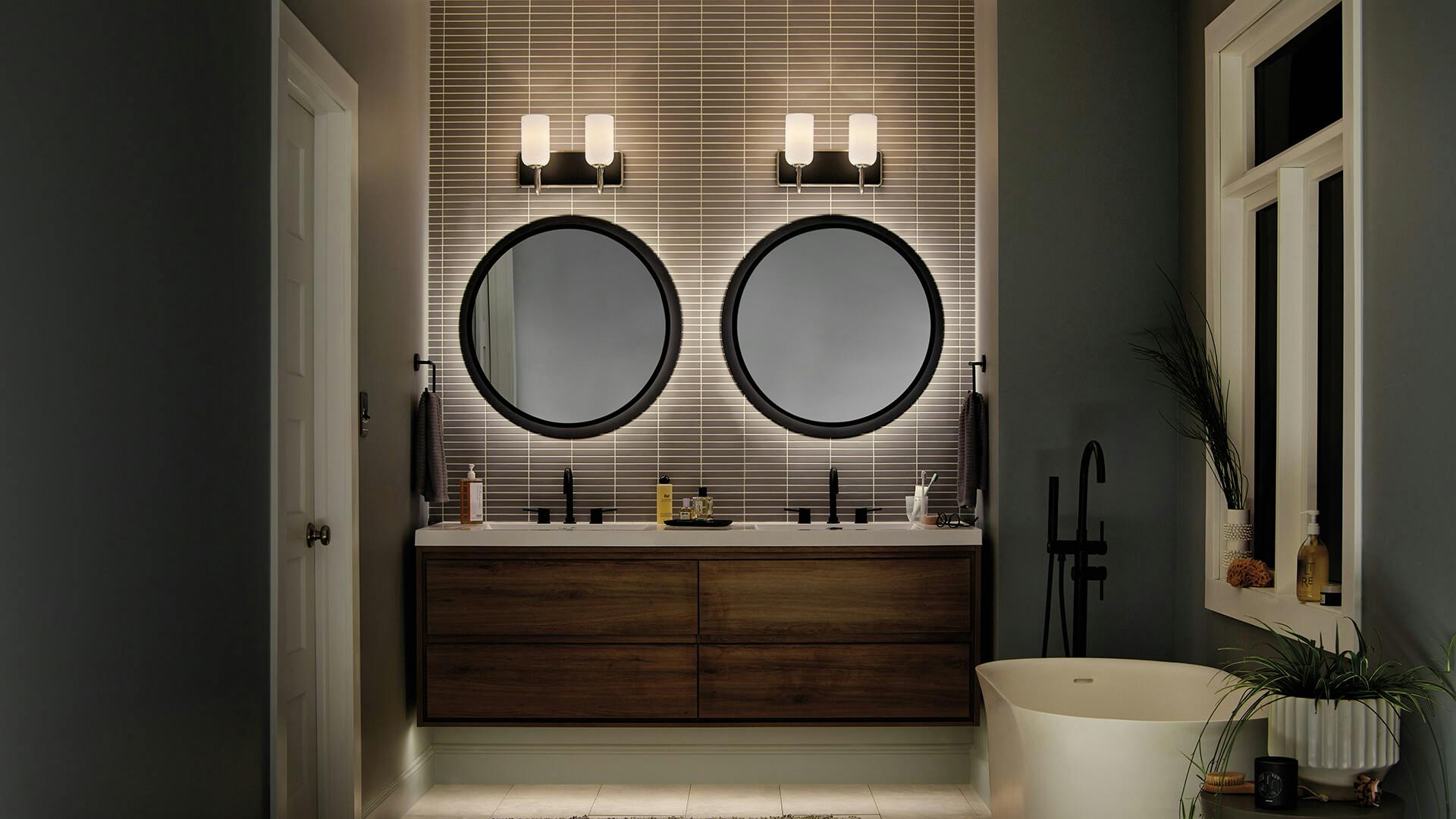 Dark bathroom at night with double vanity and two 2-light Solia vanity lights centered above two mirrors. 