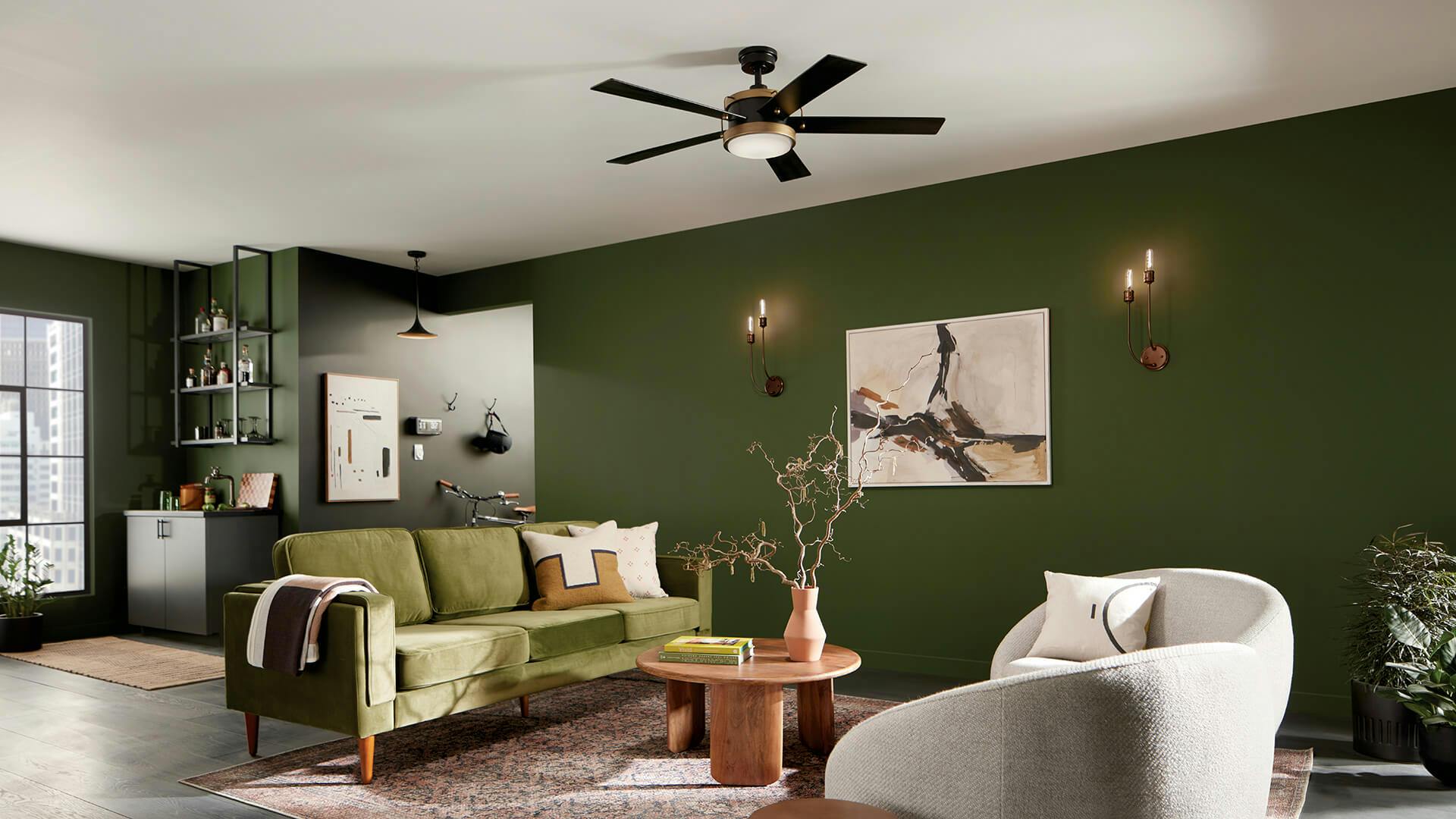 Living room at daytime featuring gold Hatton sconces lit against a deep green wall with a black and gold Salvo ceiling fan hanging above