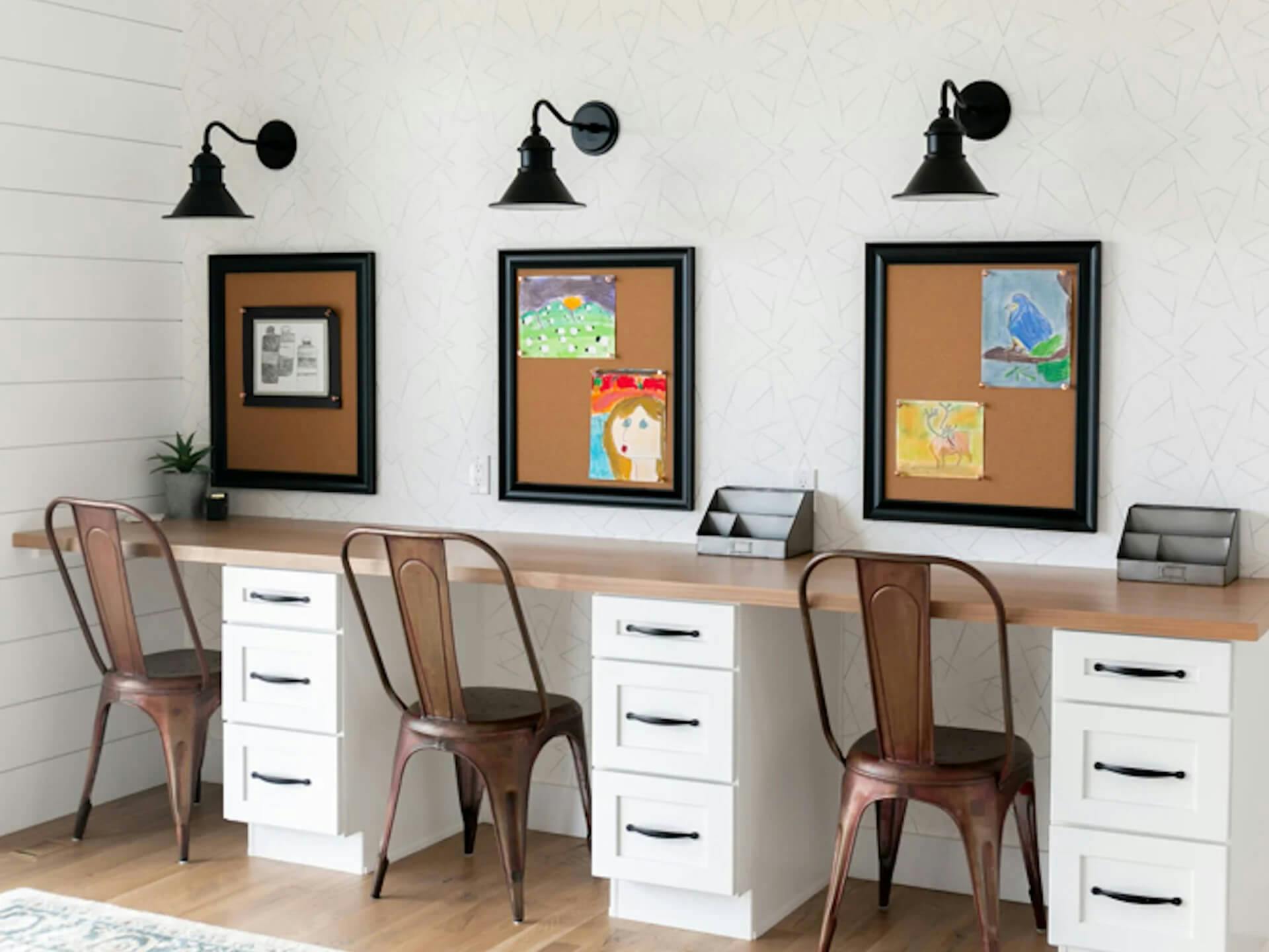 Built in desks against a wall with corkboards of children's art and Gowler wall sconces above each