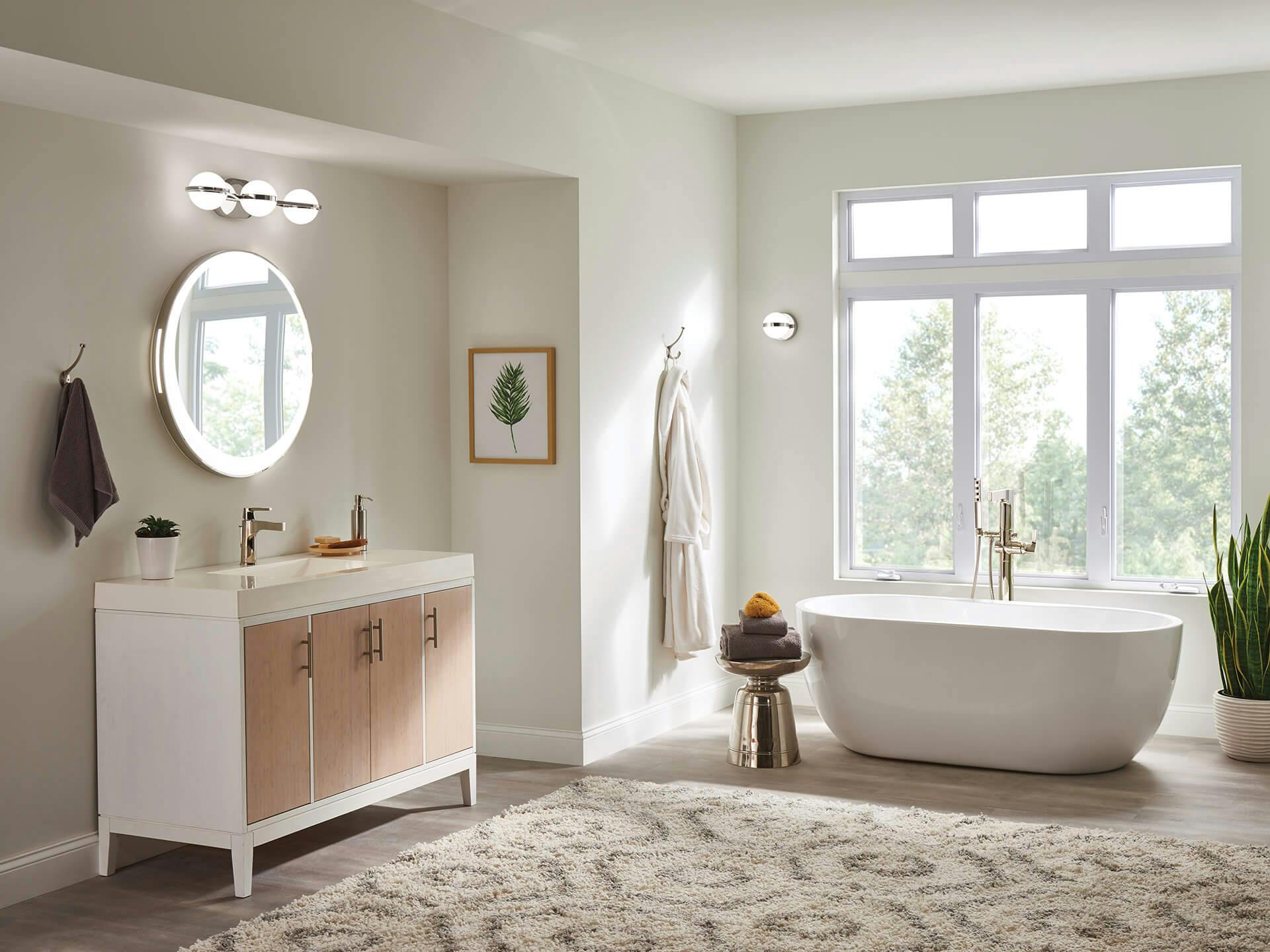 A spacious bathroom with large windows pouring in sunlight featuring Brettin vanity lights above a round mirror