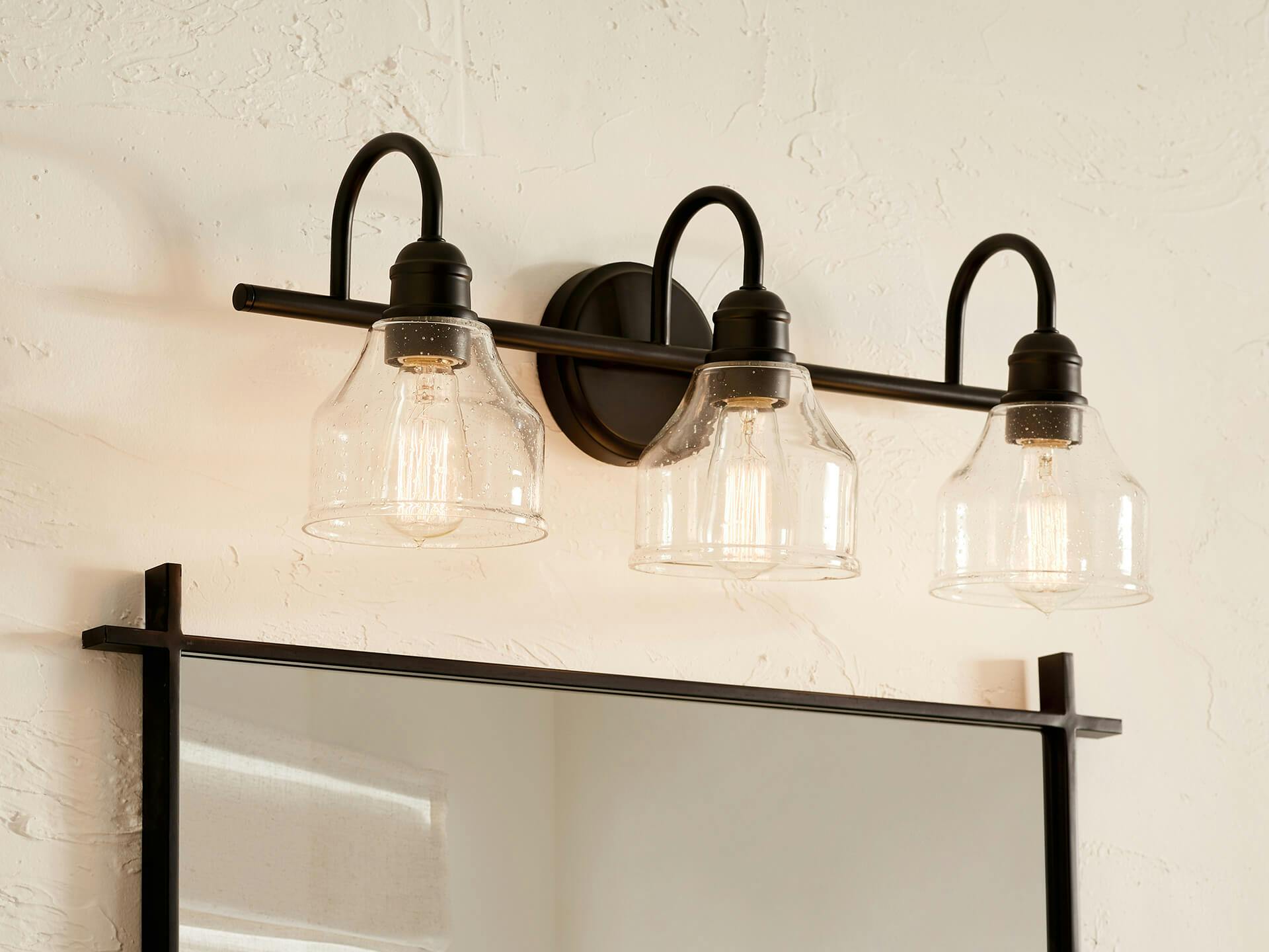 A close up of an Avery three bulb vanity light with black finish above a mirror