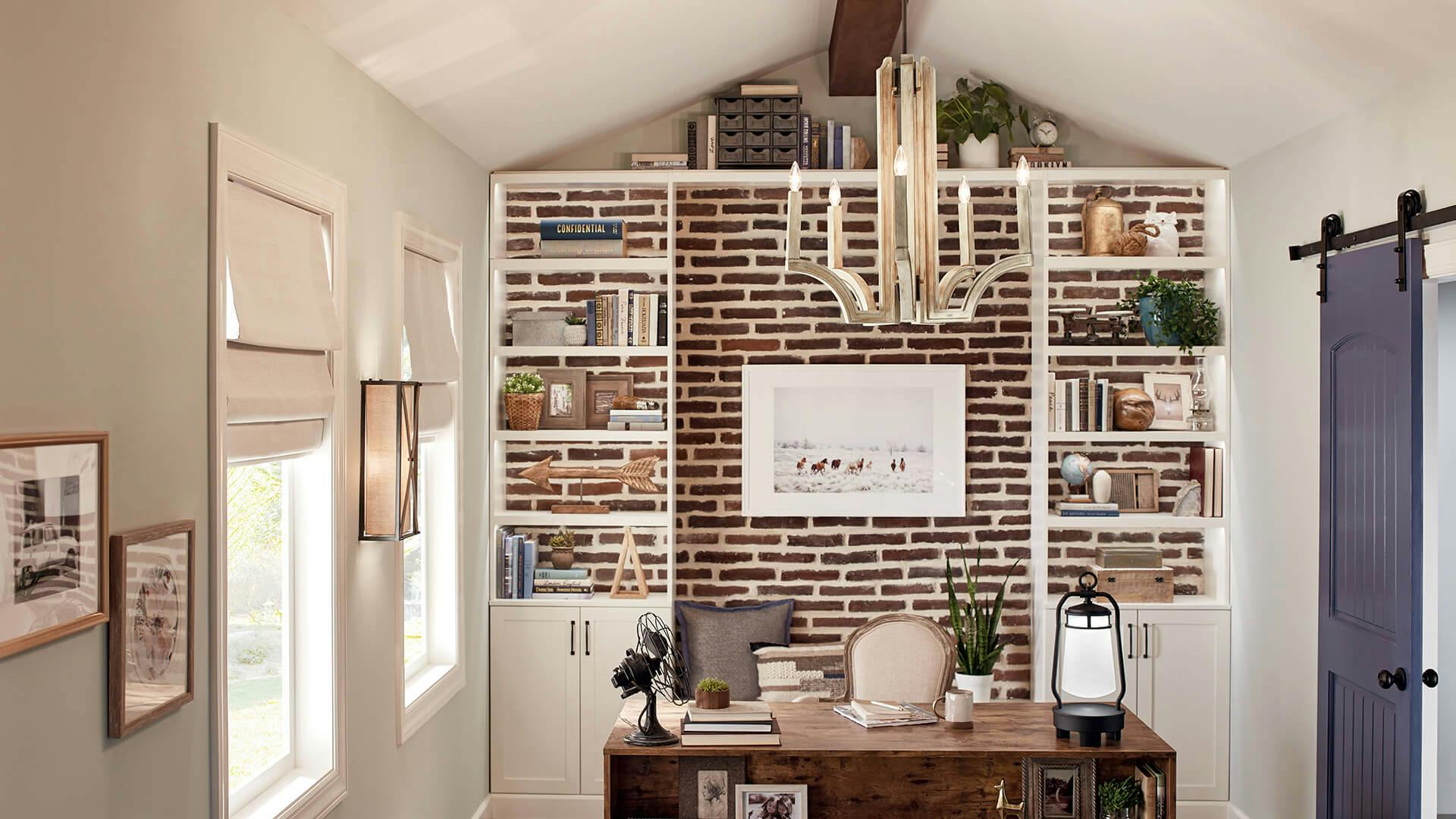 Office at daytime with light flowing through the windows on a desk against a brick wall with a Botanica chandelier lit above and Cahoon sconce on the side wall