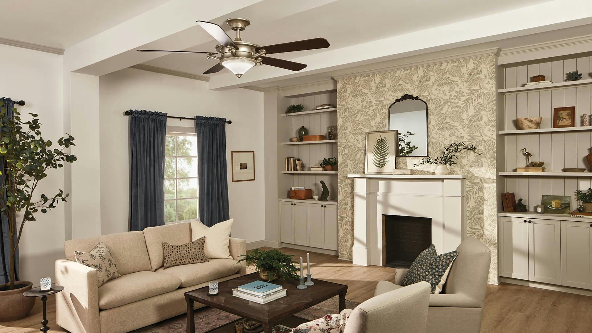 Daytime in an elegant living room with bookshelves and a fireplace in the back wall while a Rise ceiling fan hangs above the couch