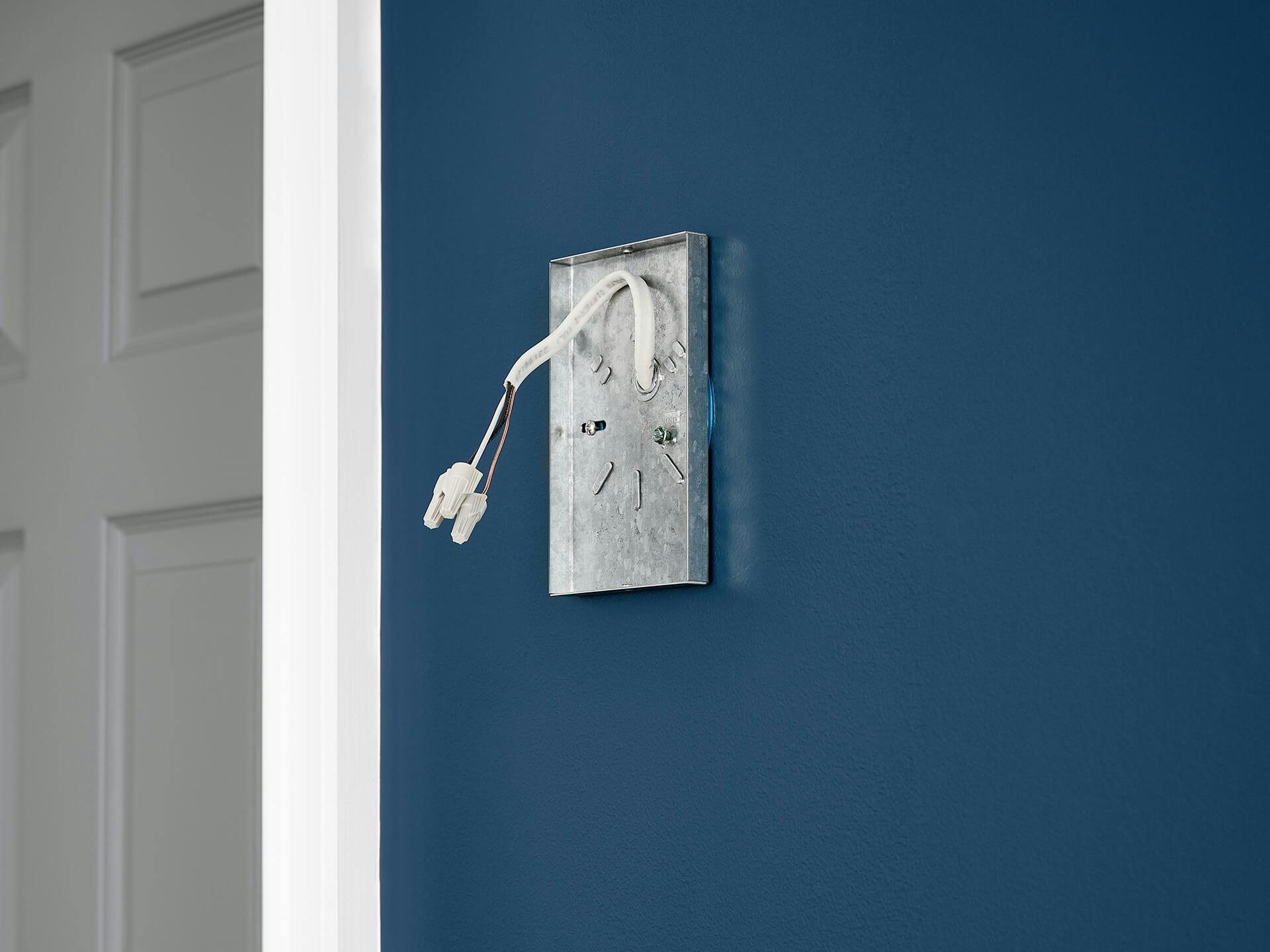 Blue wall with an example outlet box in silver and white wiring hanging loose