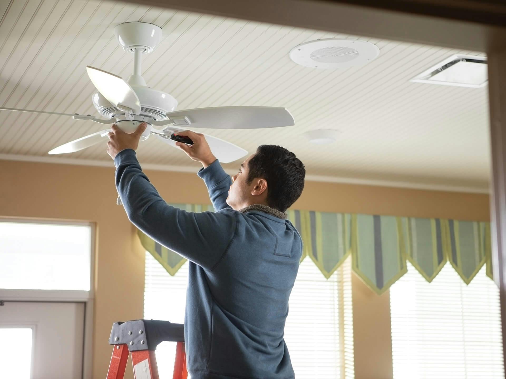 Contractor man on a ladder installing a white ceiling fan