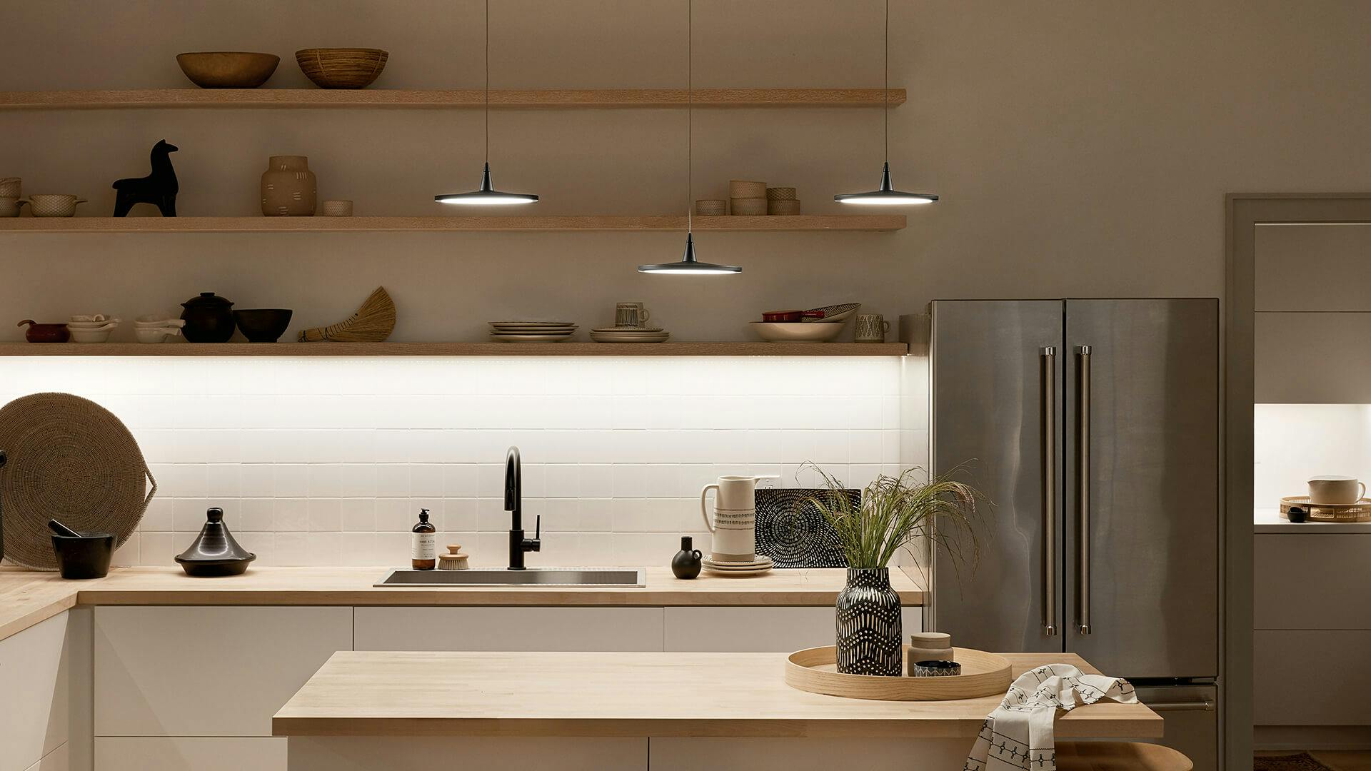 Modern kitchen with three jeno pendant lights over a maple kitchen island and shelves with tape lights.