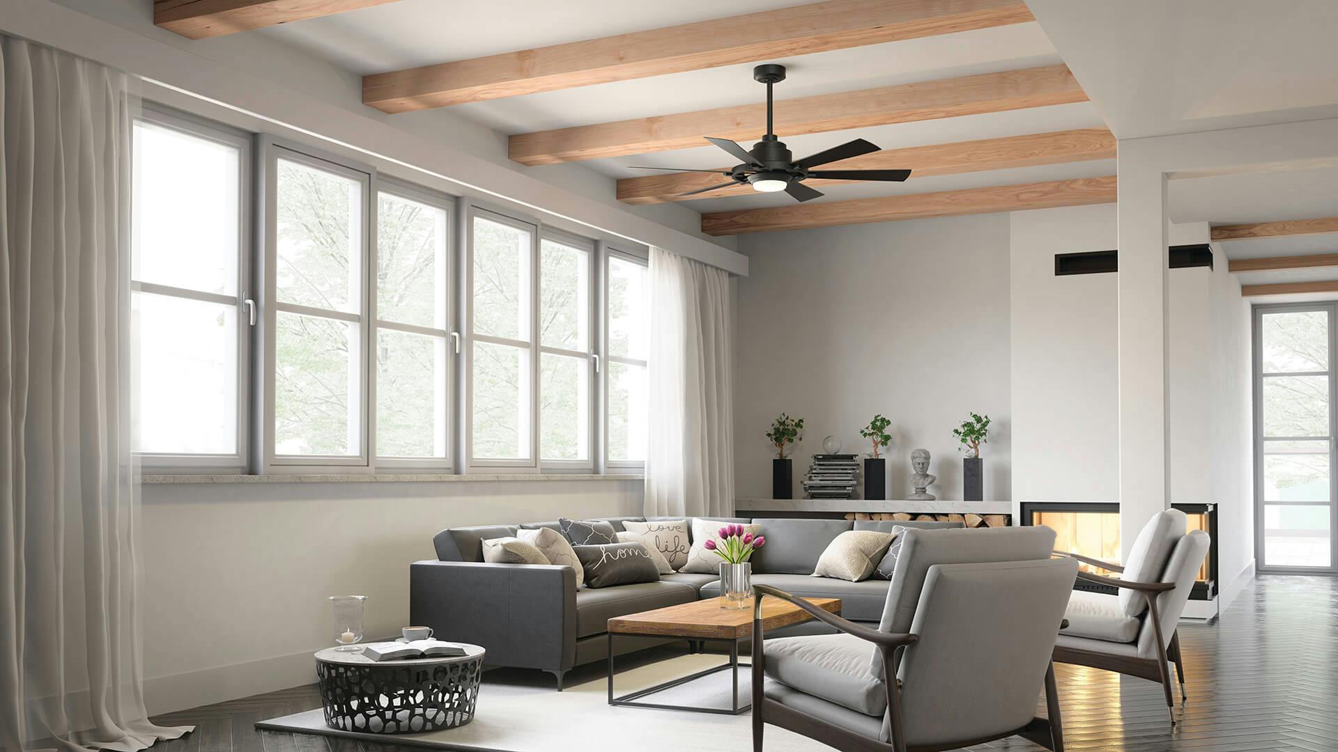 Daytime in a gray living room featuring a flat, vaulted ceiling with wooden beams while a black Iras ceiling fan hangs above a couch and set of chairs