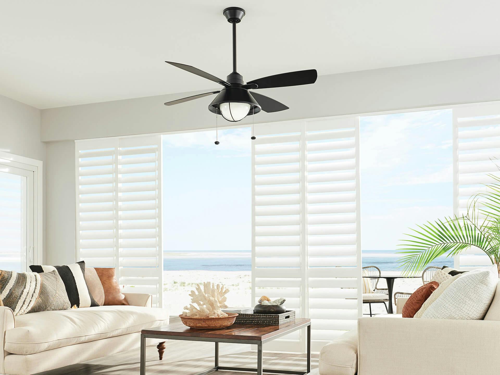 Beachside sunroom with white couches and ceiling fan