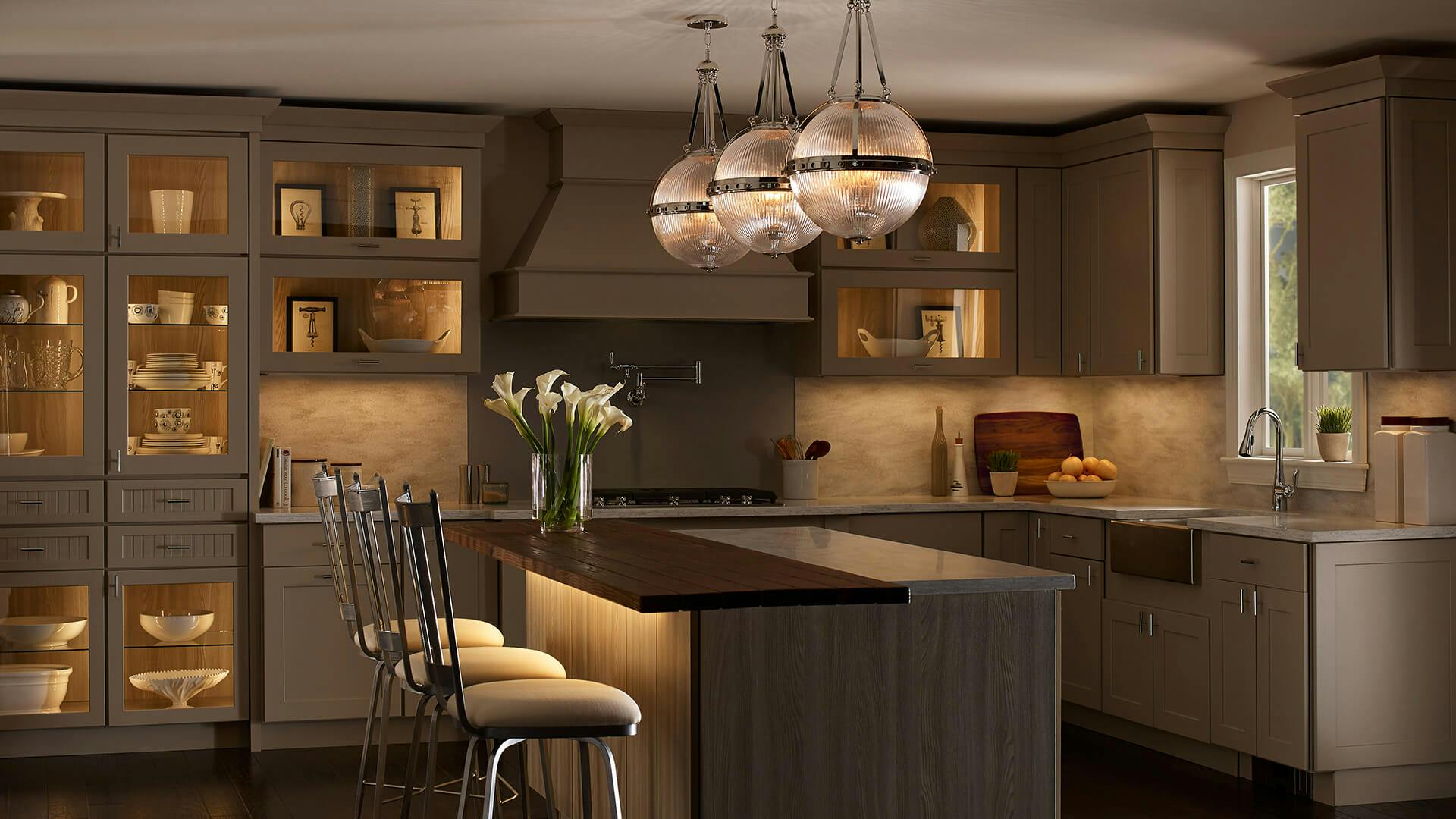 Warm, day-lit kitchen with three Aster pendants lit above the island with additional lighting under the countertop 