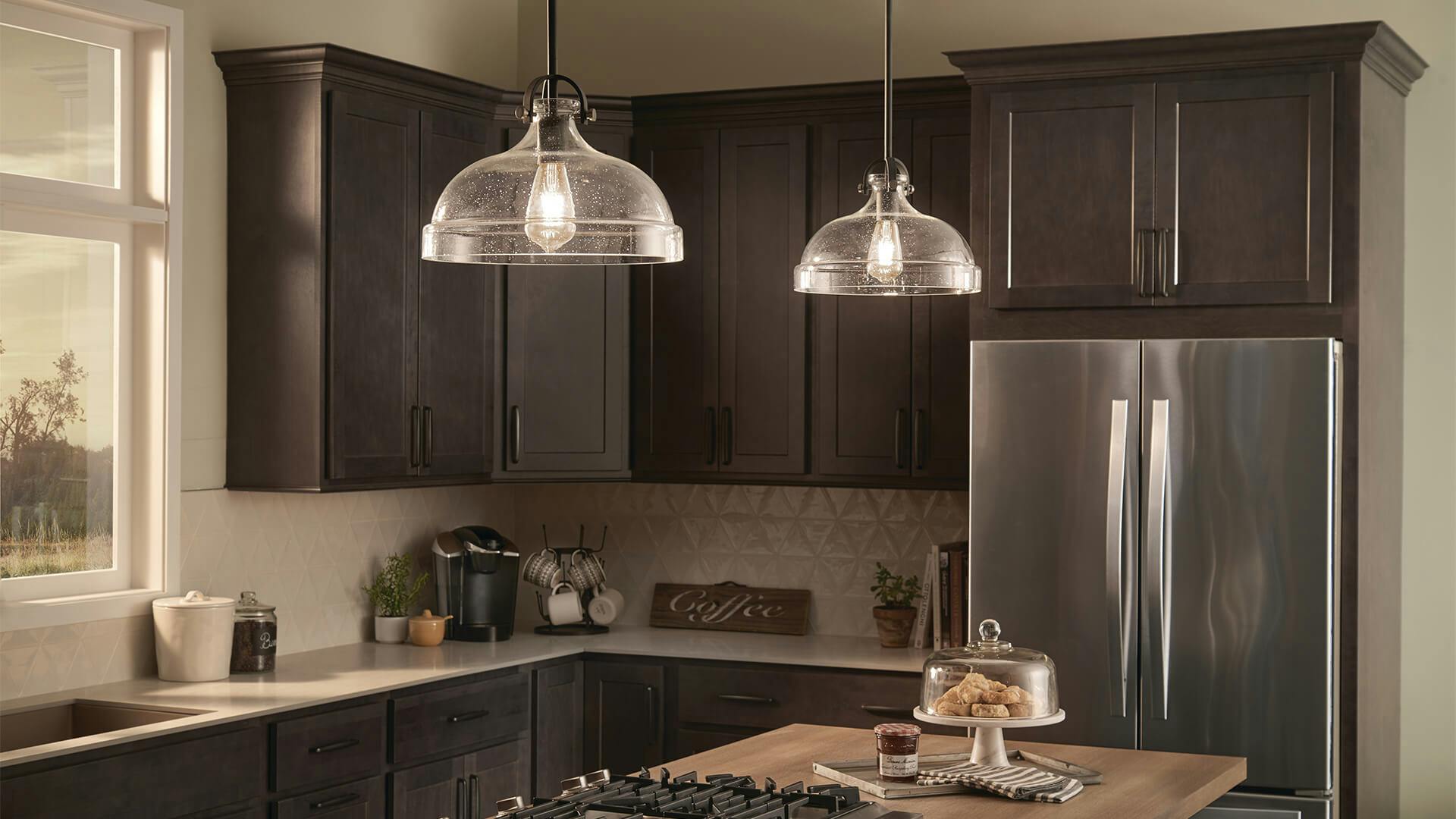 A kitchen with two glass pendant lights turned on above a kitchen island during the day