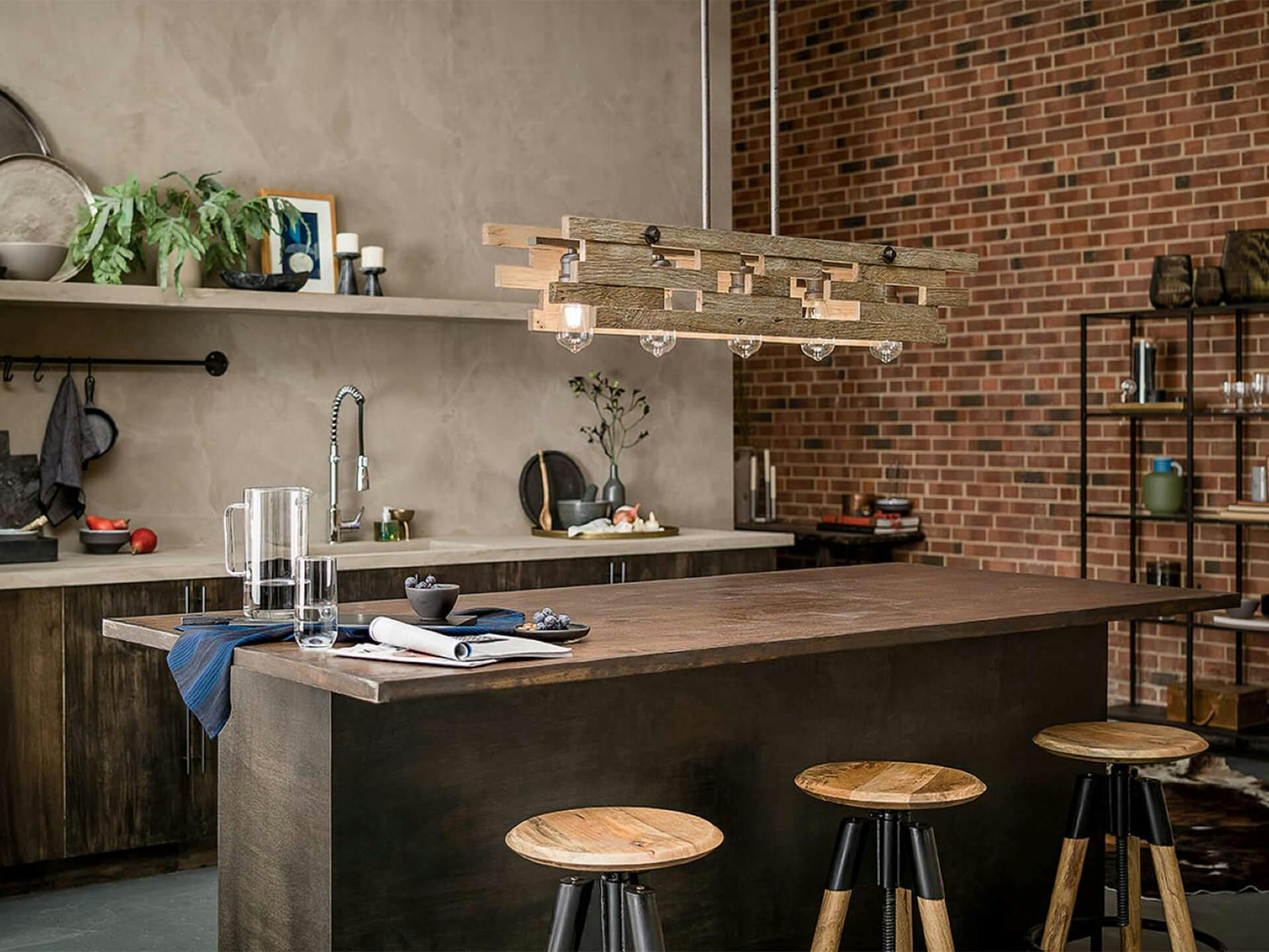 Industrial kitchen with brick wall, metal shelves, long kitchen island and featuring a Cuyahoga Mill chandelier in a light wood