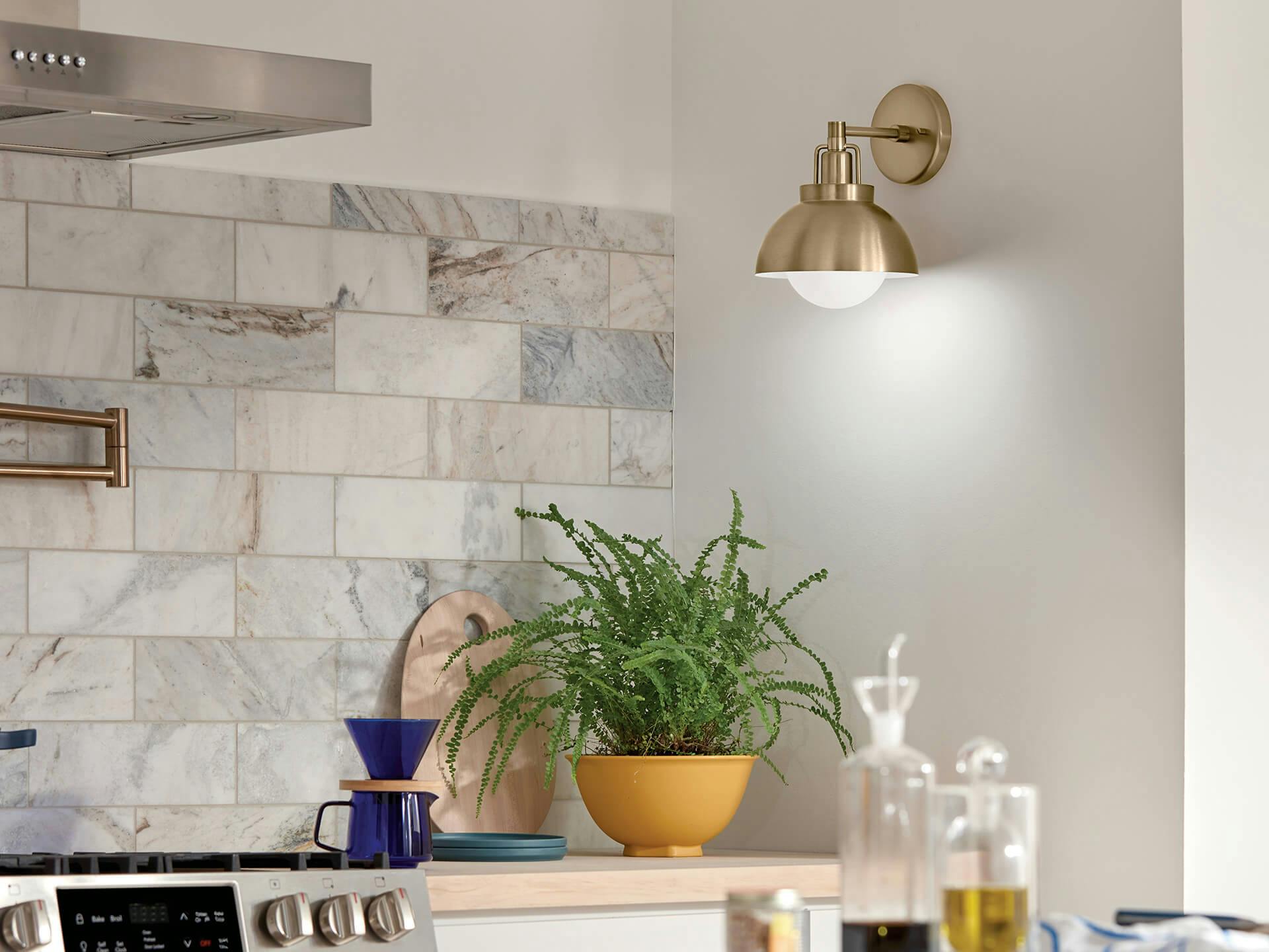 Kitchen focused on a Niva sconce in champagne bronze illuminating the countertop below