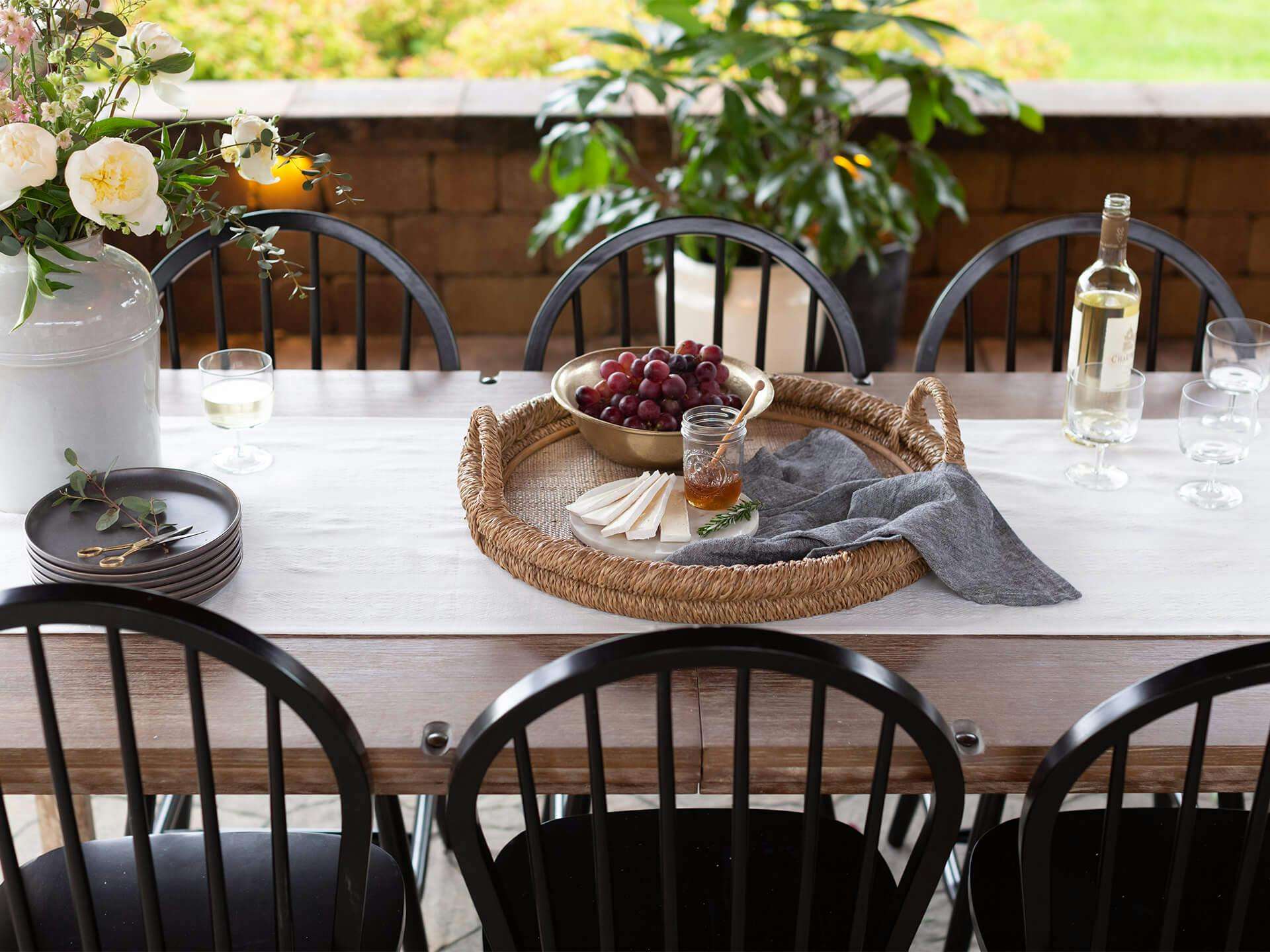 an outdoor table set with a cheese and grape platter