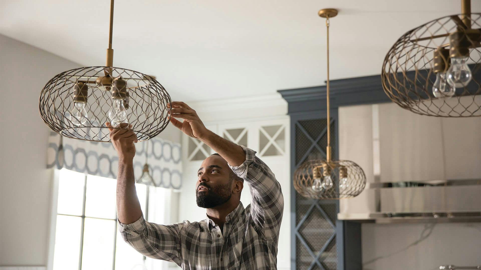 Man installing a chandelier light in a kitchen.
