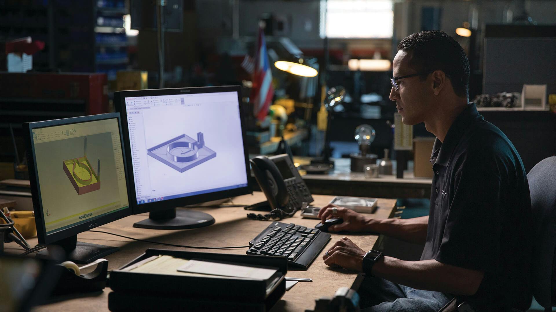 Man wearing polo inside office with technical design images on his computer monitors