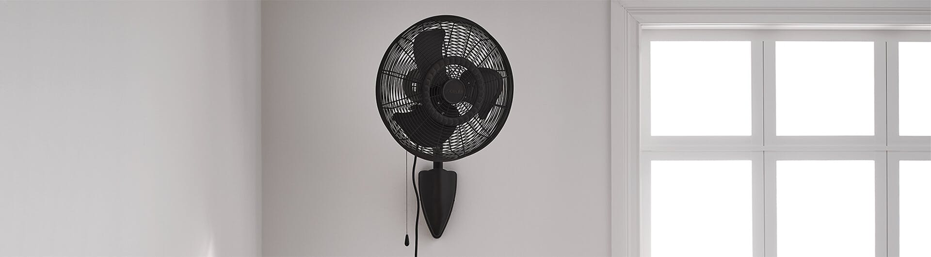 Pola wall fan in natural bronze mounted next to a daylit bedroom window