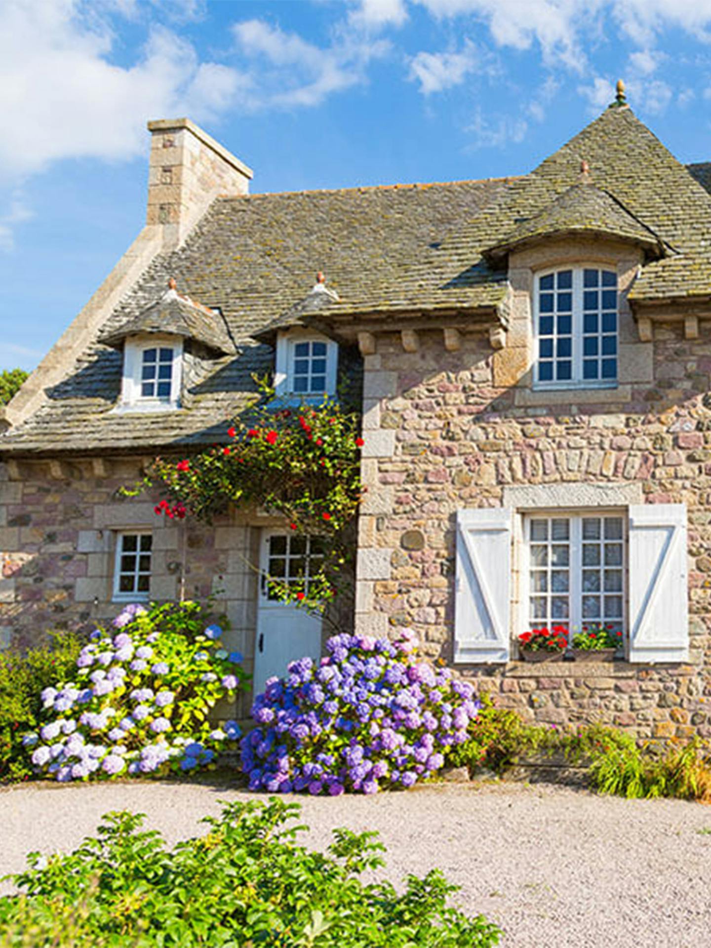 Exterior of a stone cottage surrounded by flowers during the day