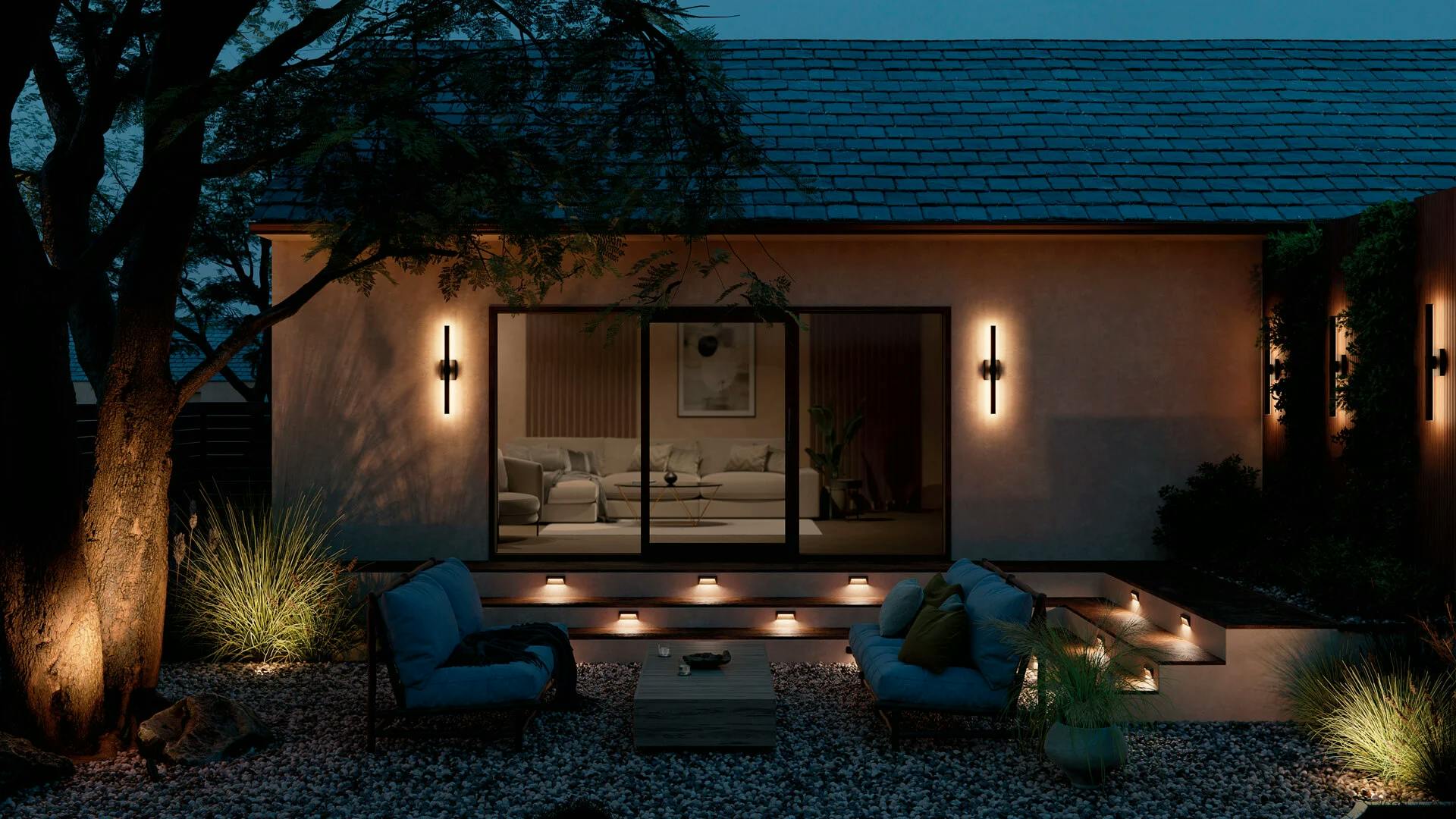 A back yard at night featuring step lights and nocar wall sconces in black.