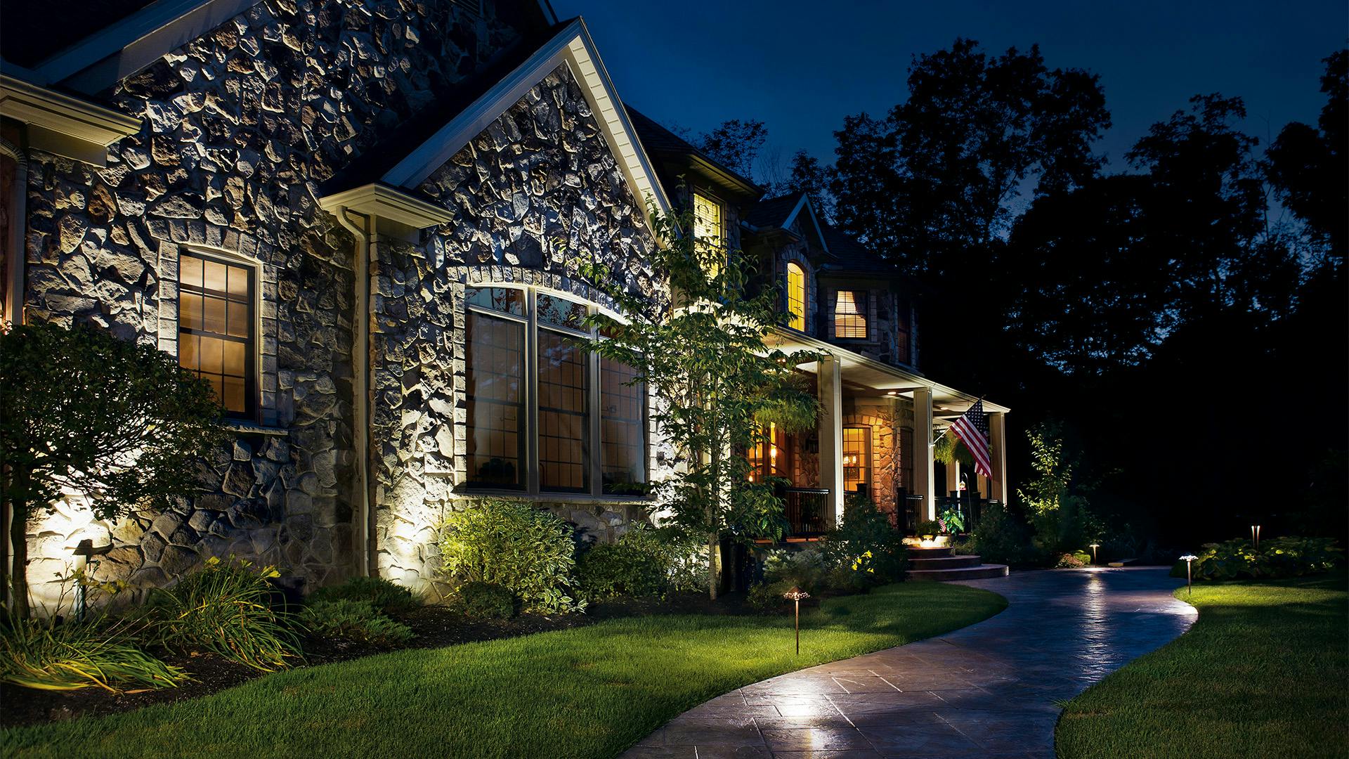 Exterior of a stone home at night with variety of path lights and uplighting