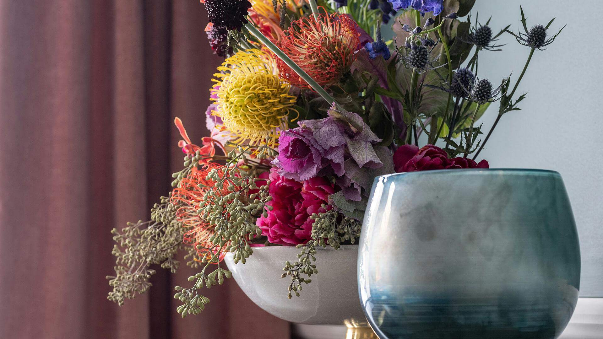 Close up of a bouquet of various jewel tone flowers and a glass vase